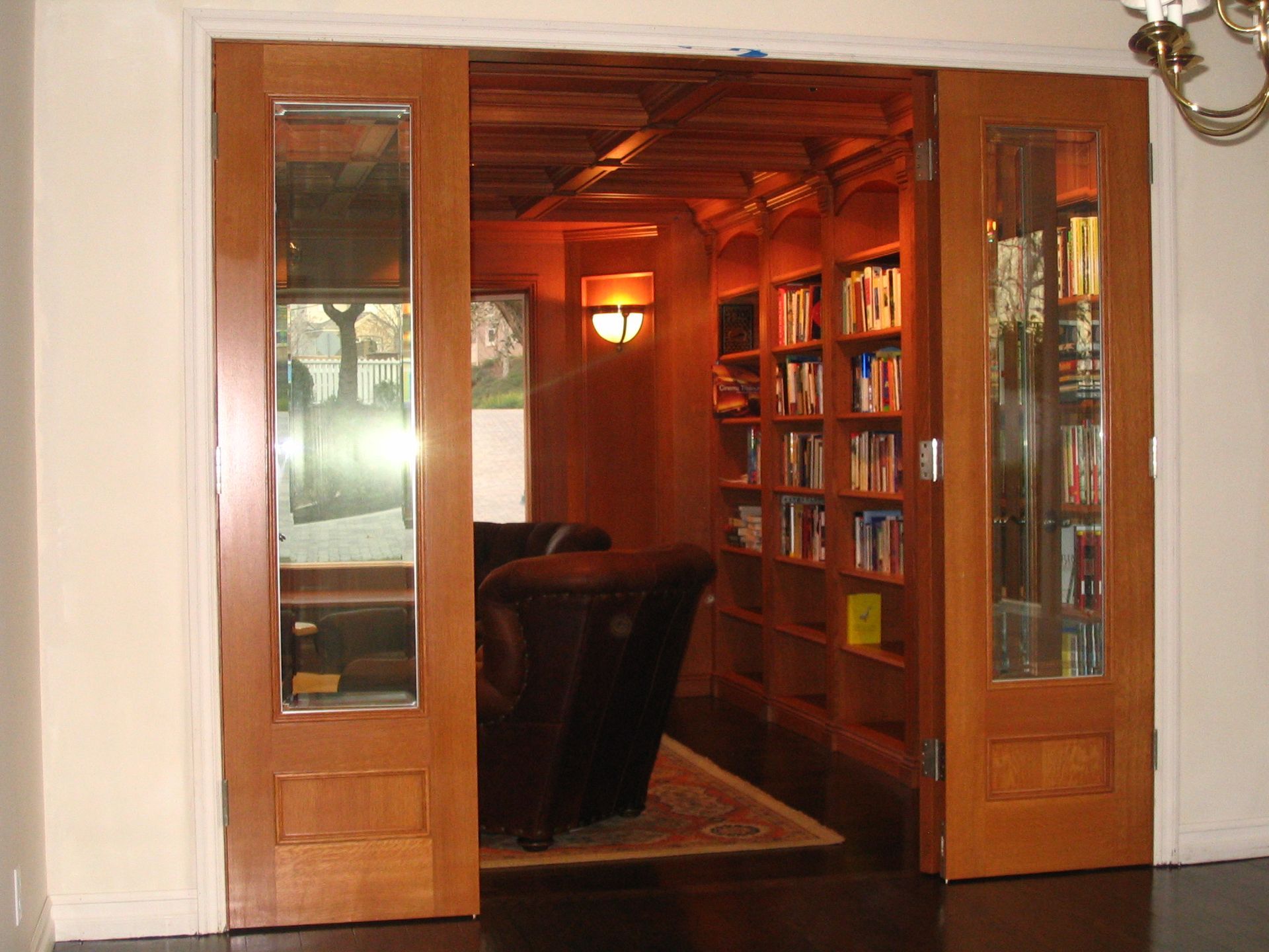 Wooden double doors open into a library with bookshelves and a leather chair.