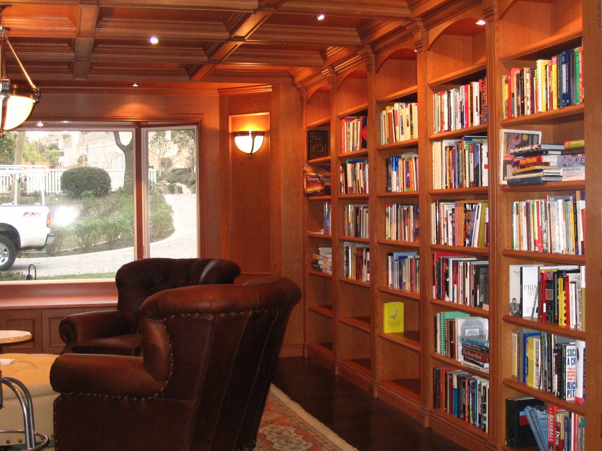 Cozy library with built-in wooden bookshelves filled with books, leather armchairs, and a window overlooking a street.