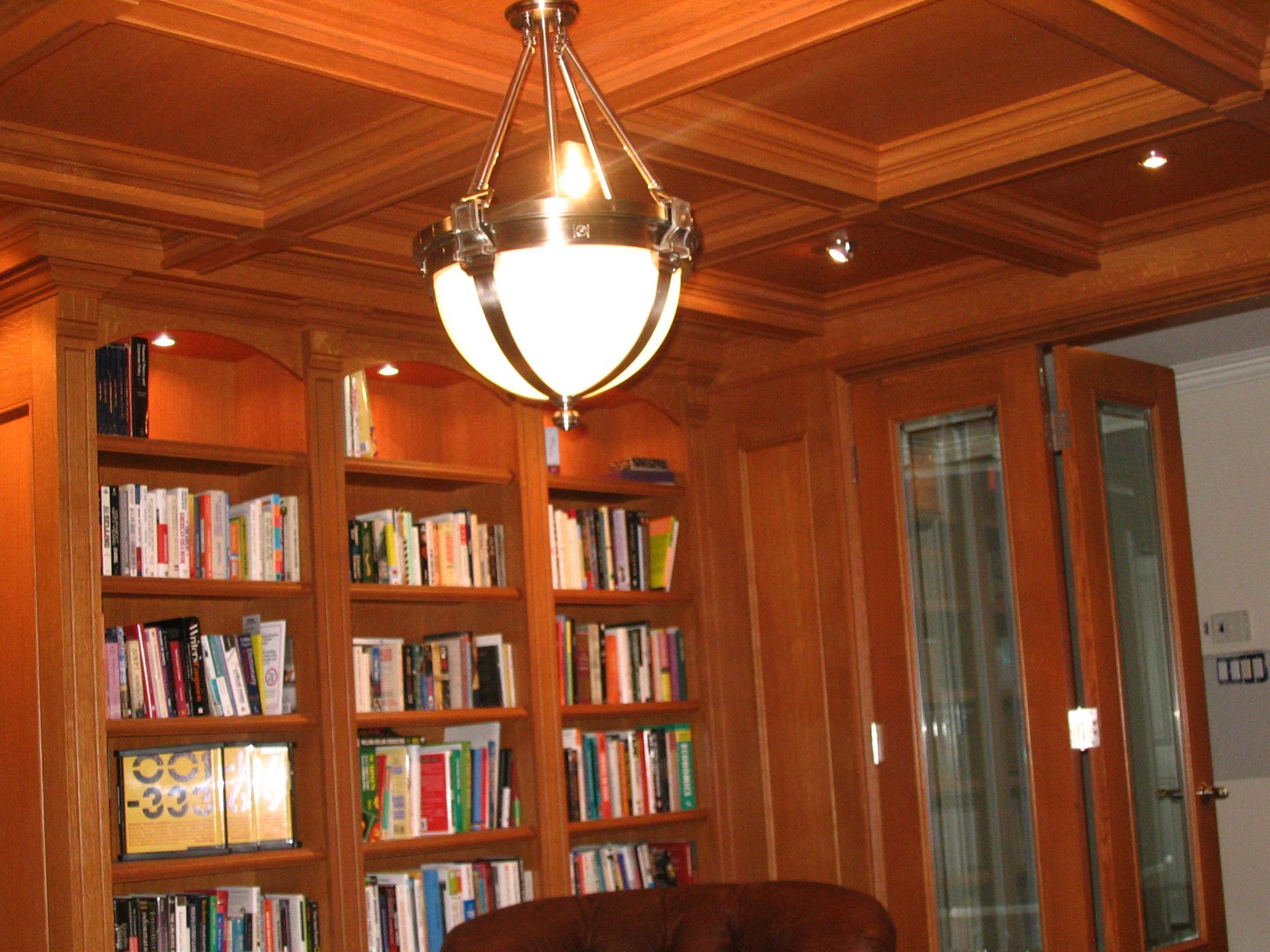 Wooden library with bookshelves, books, and a hanging light fixture.