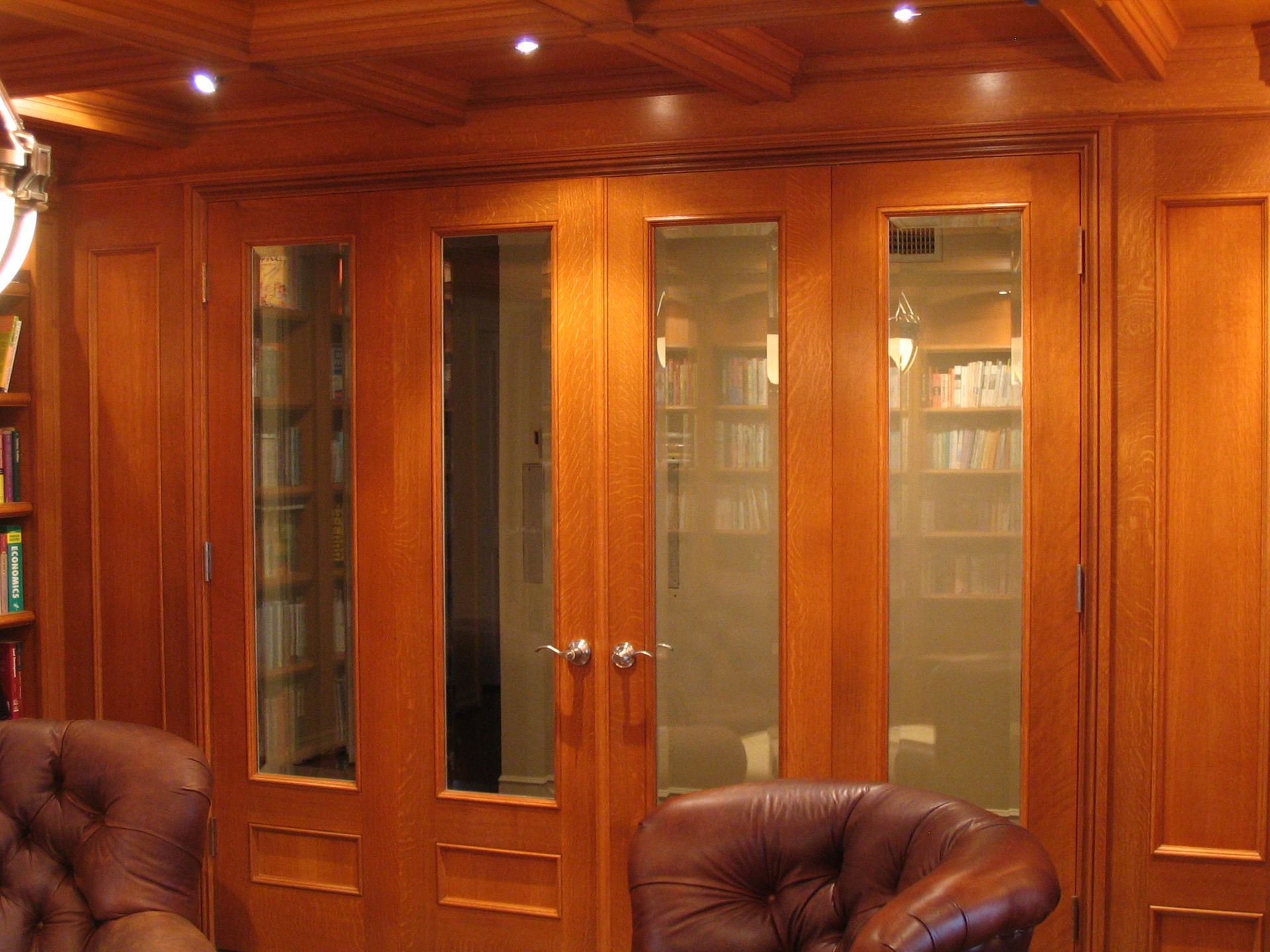 Wooden double doors with glass panels leading to a library with bookshelves. Two brown leather chairs in the foreground.