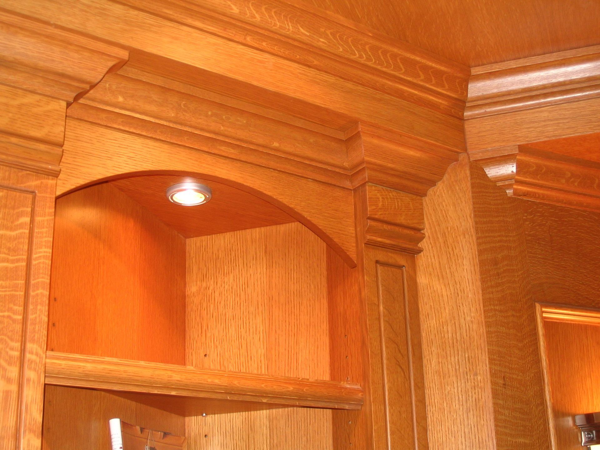 Wooden built-in cabinetry with arched niche and recessed lighting. Warm, natural wood tones.