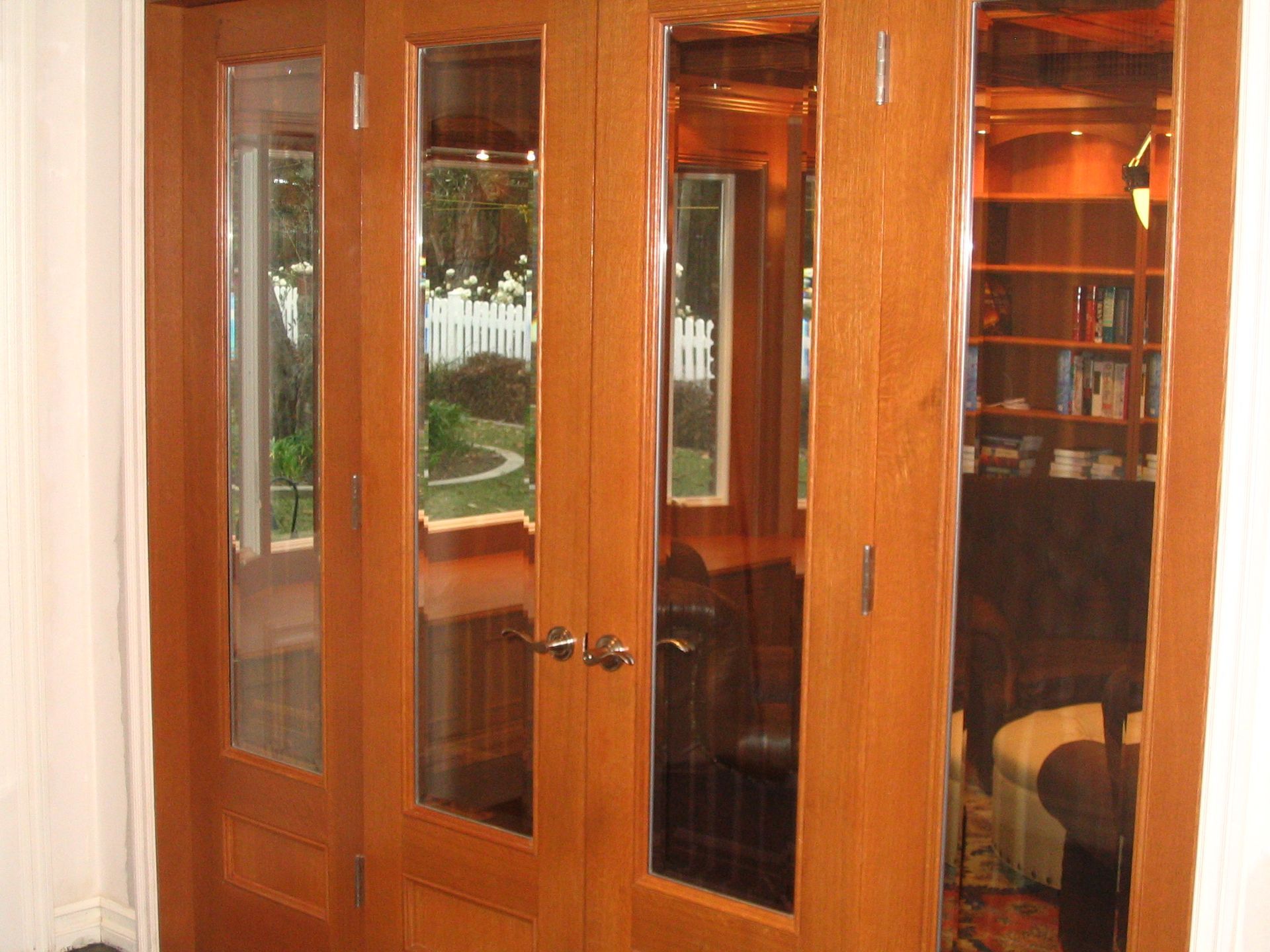 Wooden double doors with glass panels, reflecting a room and outside view.