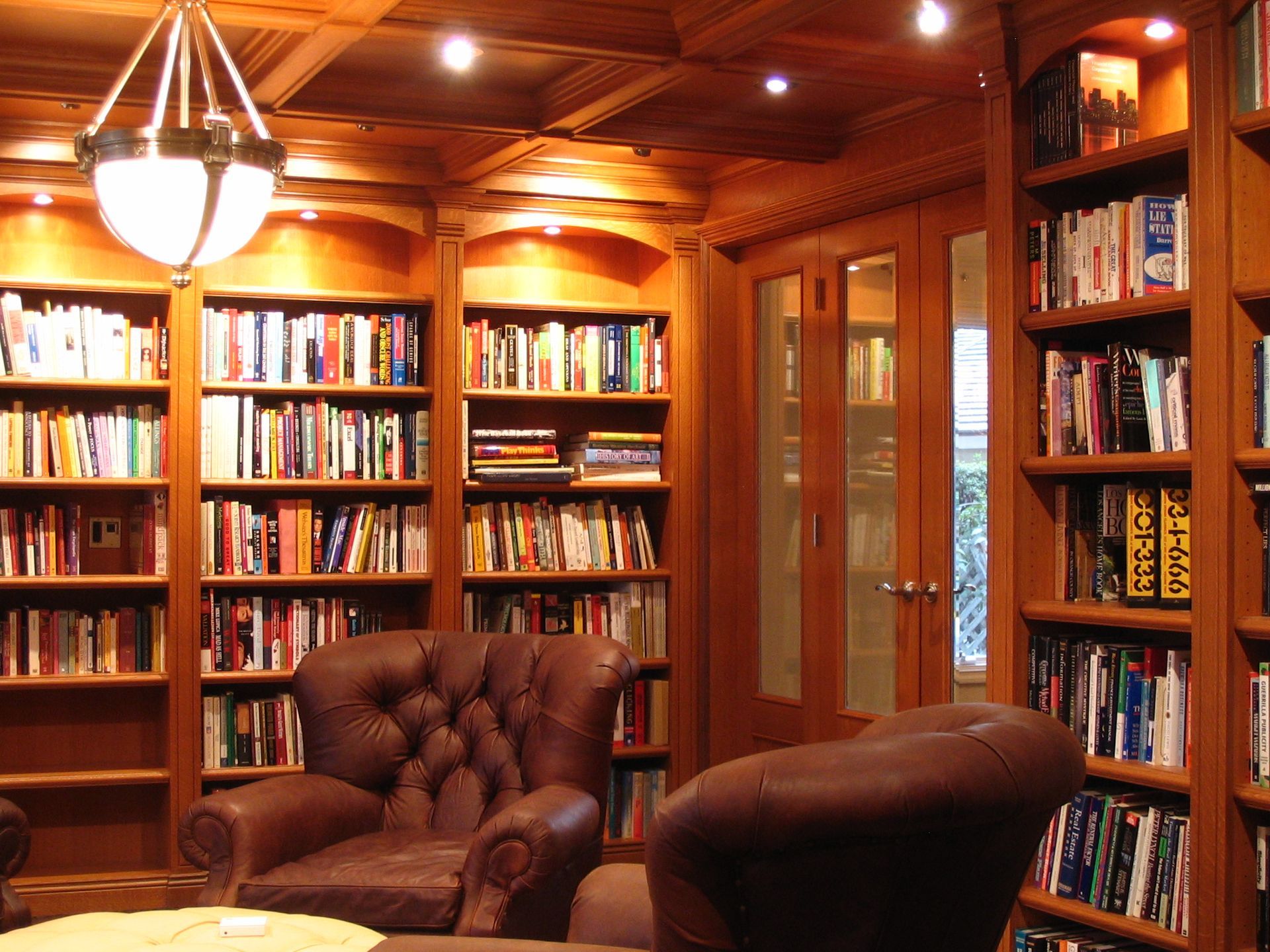 Wooden library with bookshelves filled with books, leather chairs, and a chandelier.