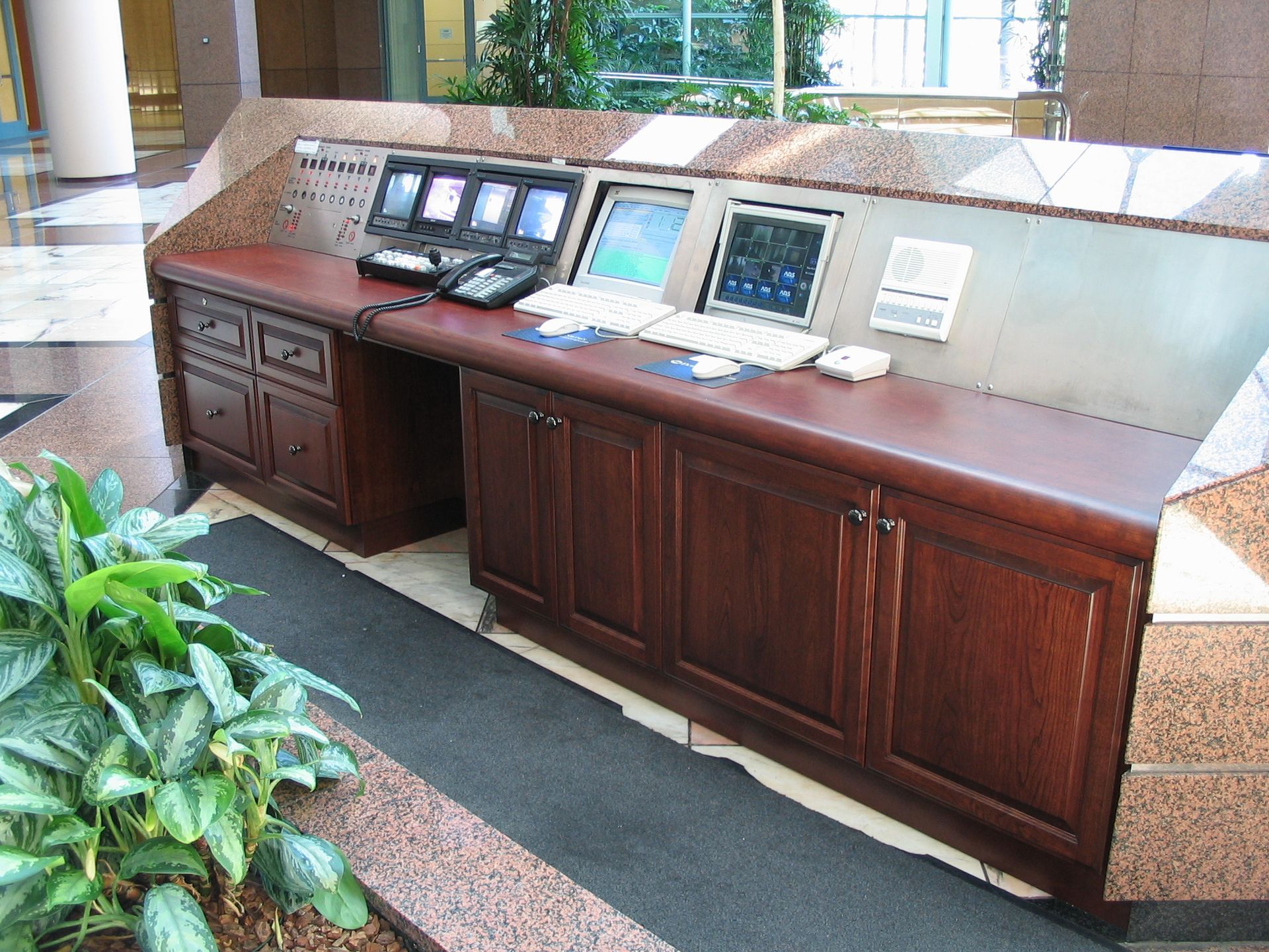 Reception desk with multiple monitors, computers, and a telephone. Wooden cabinets and a granite top.