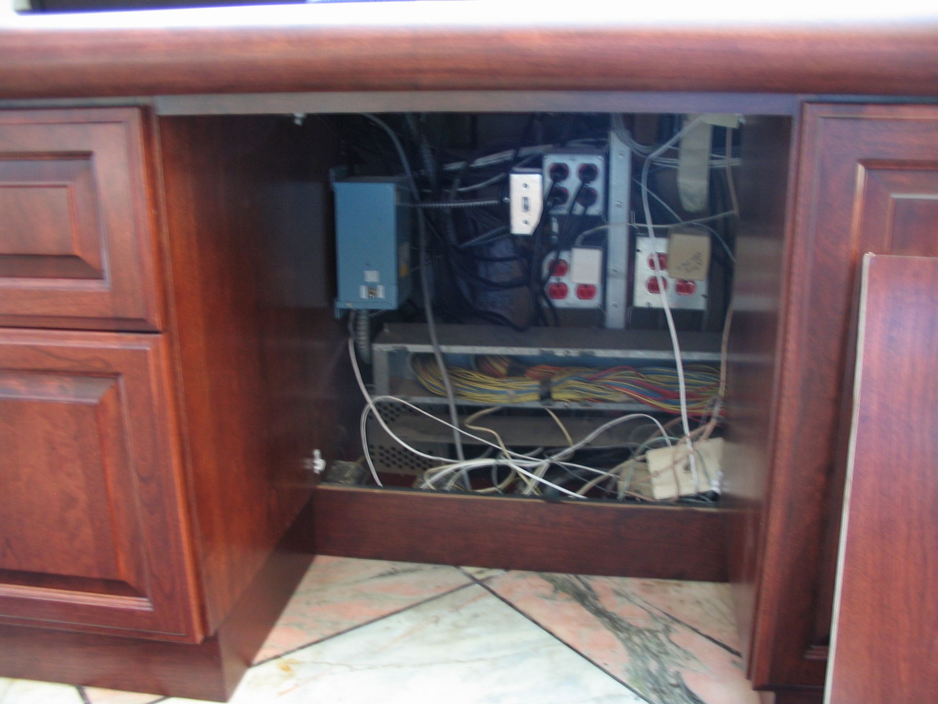 Open cabinet under counter with electrical wiring, outlets, and equipment, plus a detached cabinet door.