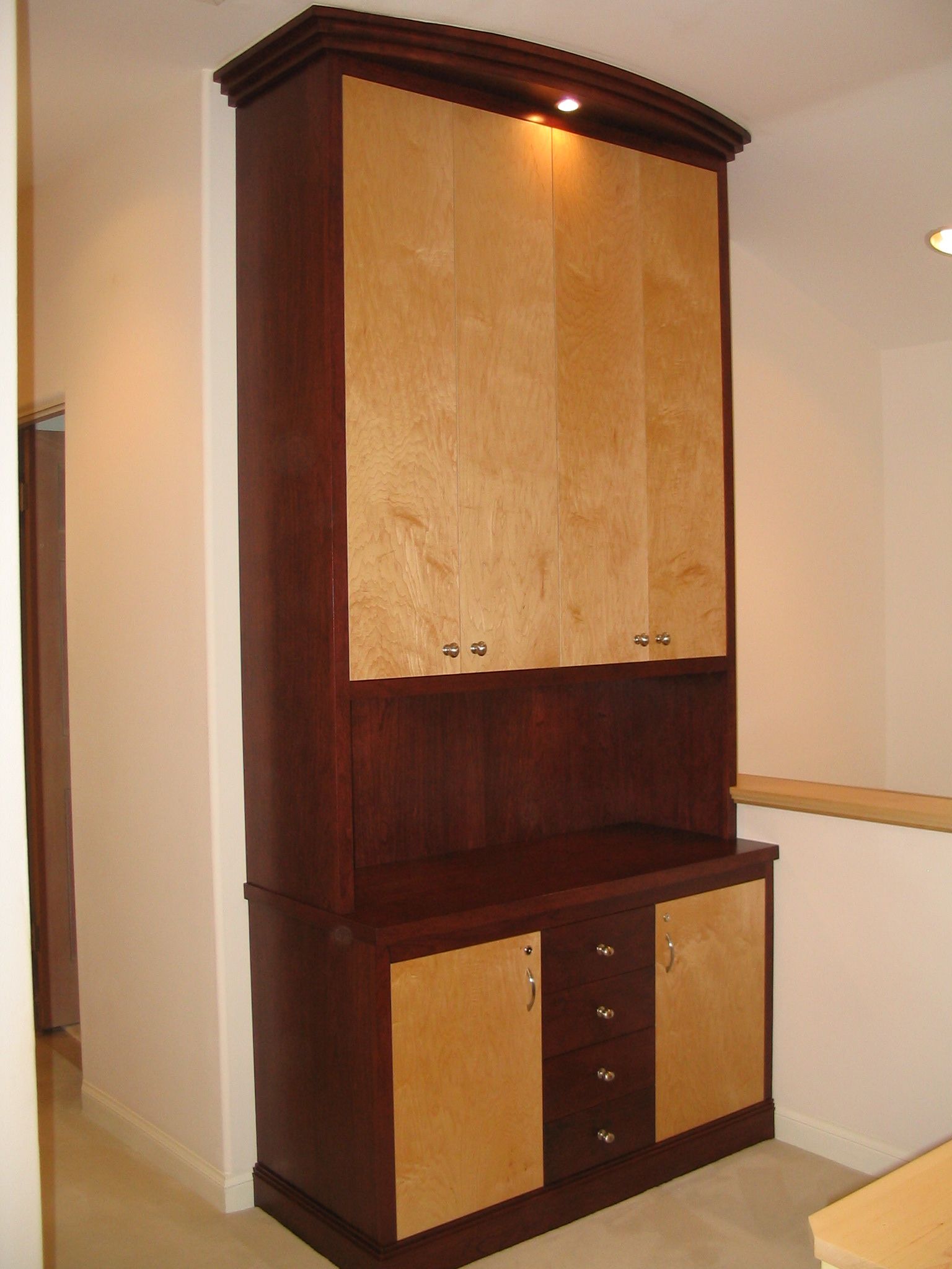 Tall wooden cabinet with light wood door panels, dark wood trim, and interior lighting.