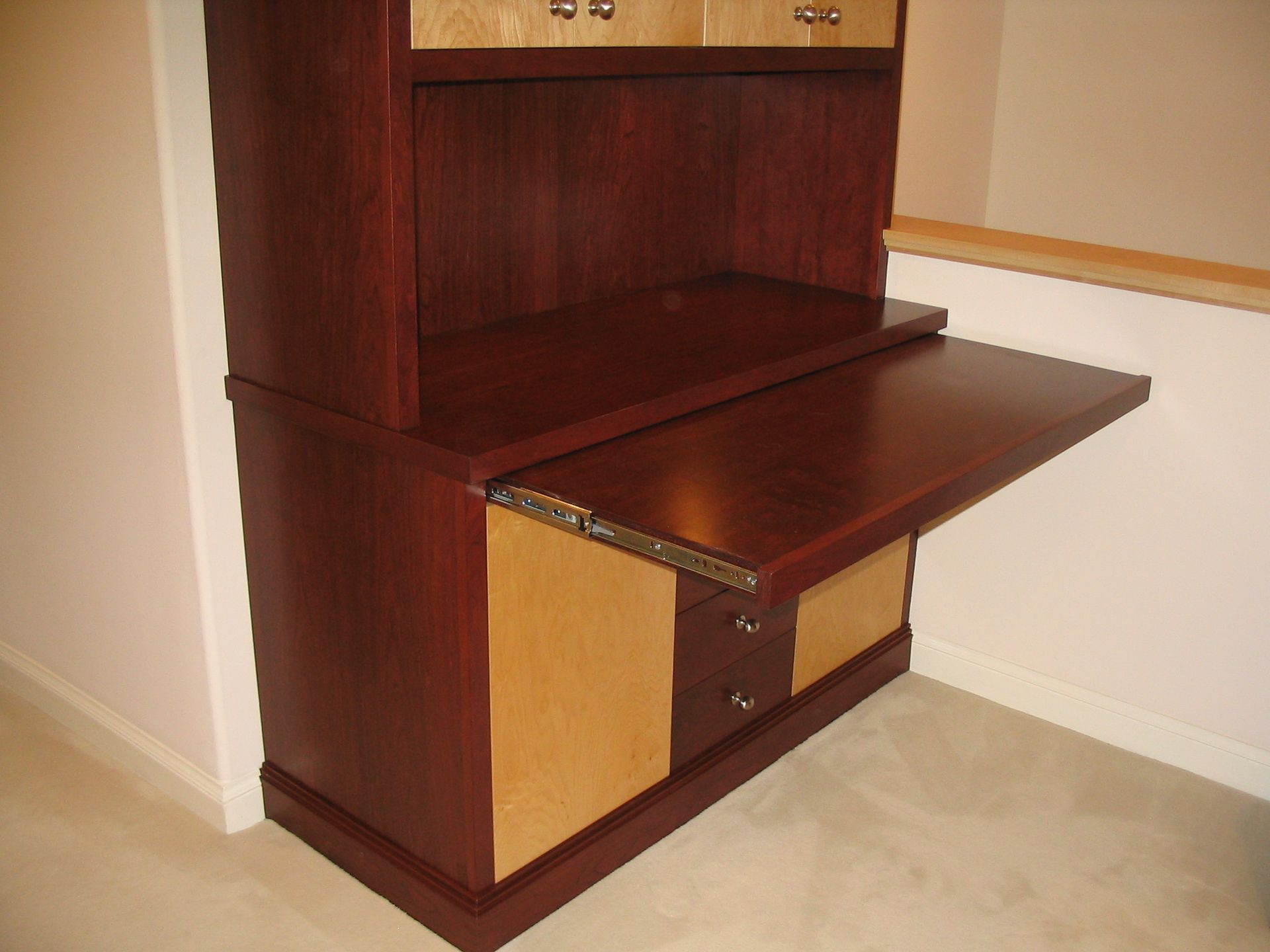 Dark wood desk cabinet with a pull-out desk surface; two-toned with light wood accents.