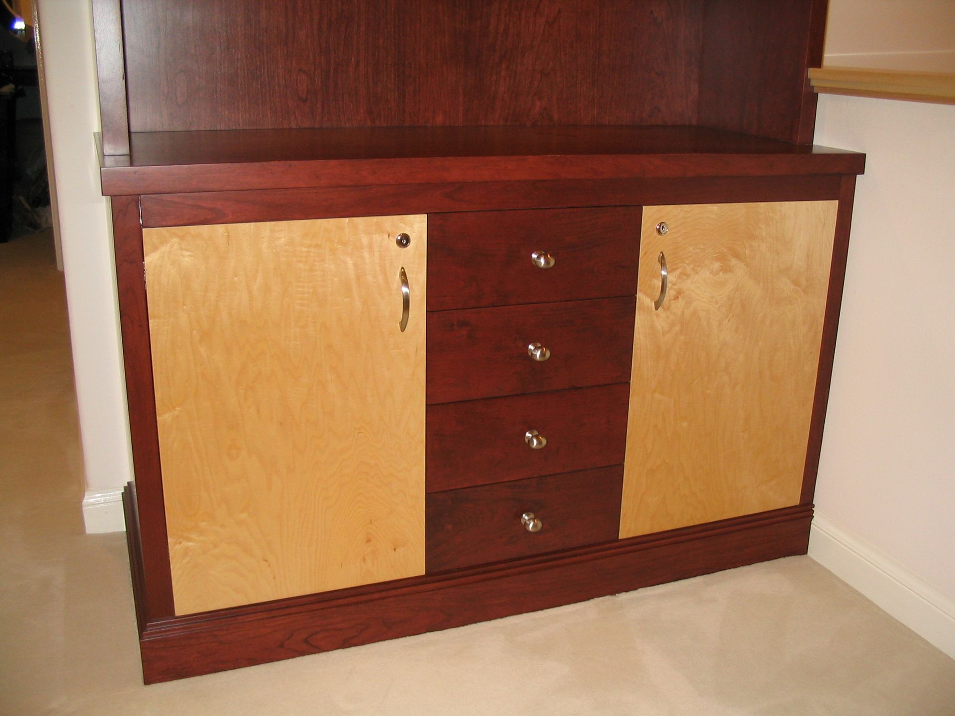 Wooden cabinet with two light doors, four dark drawers, and dark wood trim.