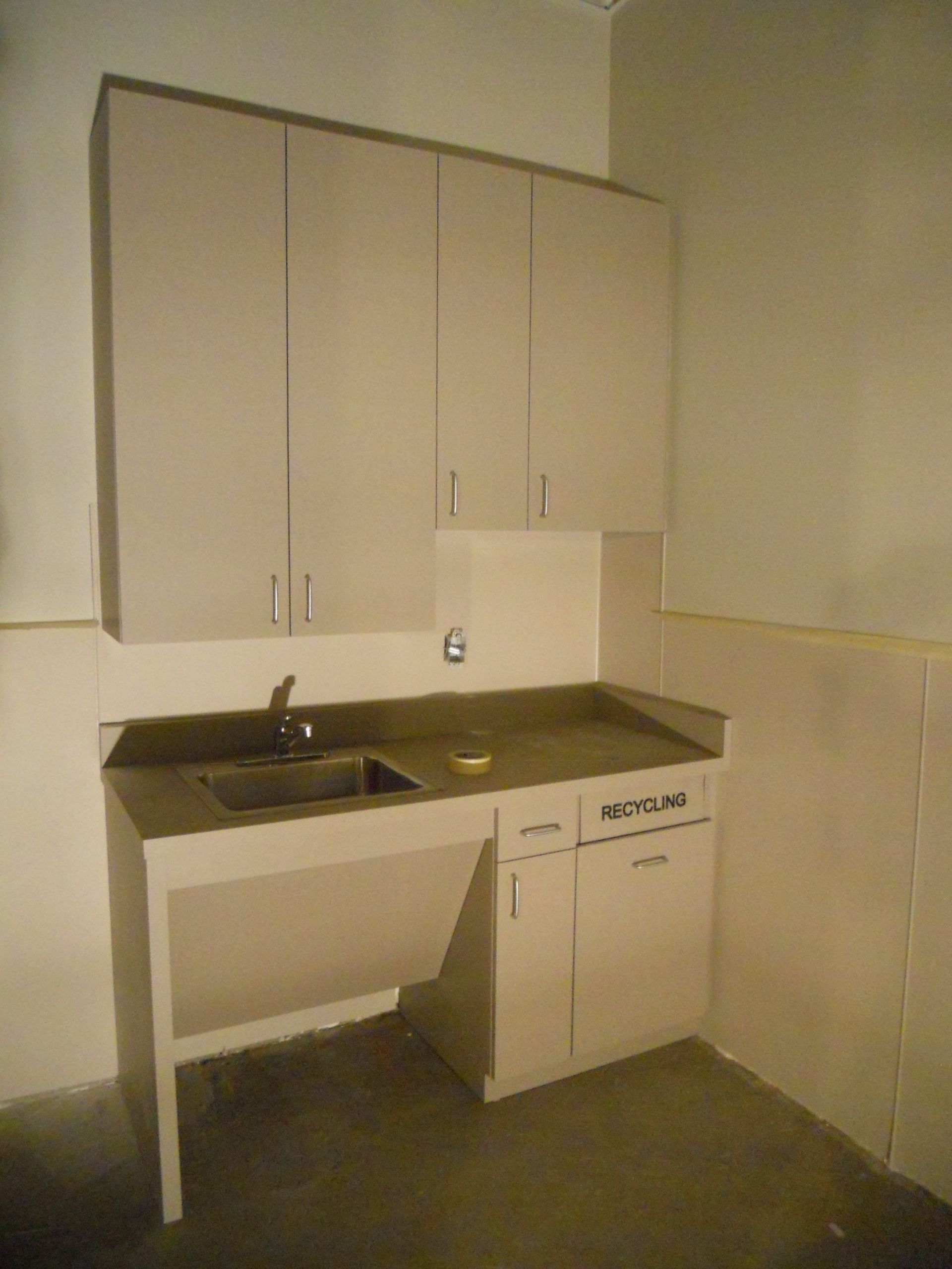 A beige accessible sink with cabinet, and upper cabinets in a corner.