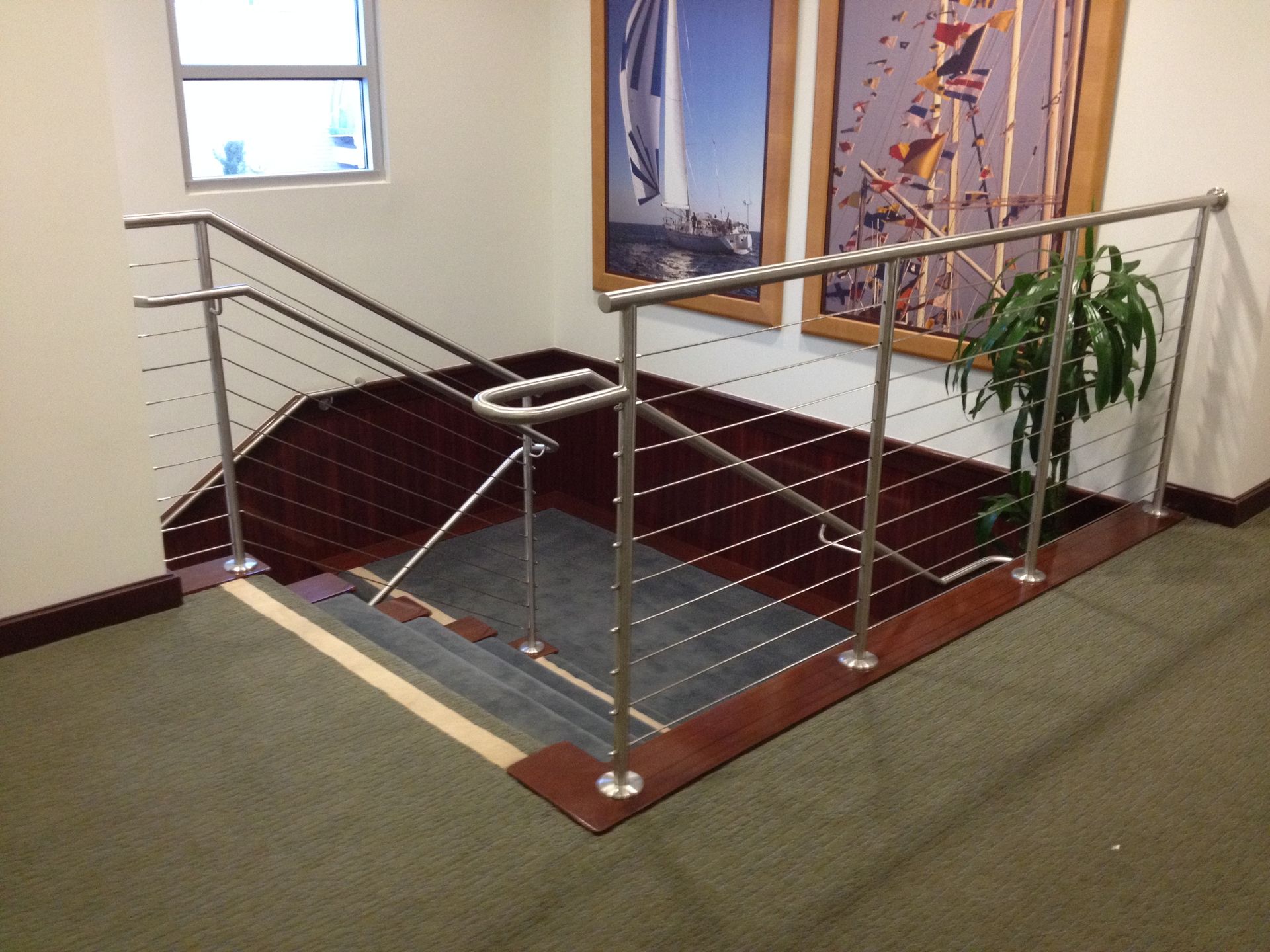 Staircase with stainless steel railing and wire, dark wood accents, and framed art.