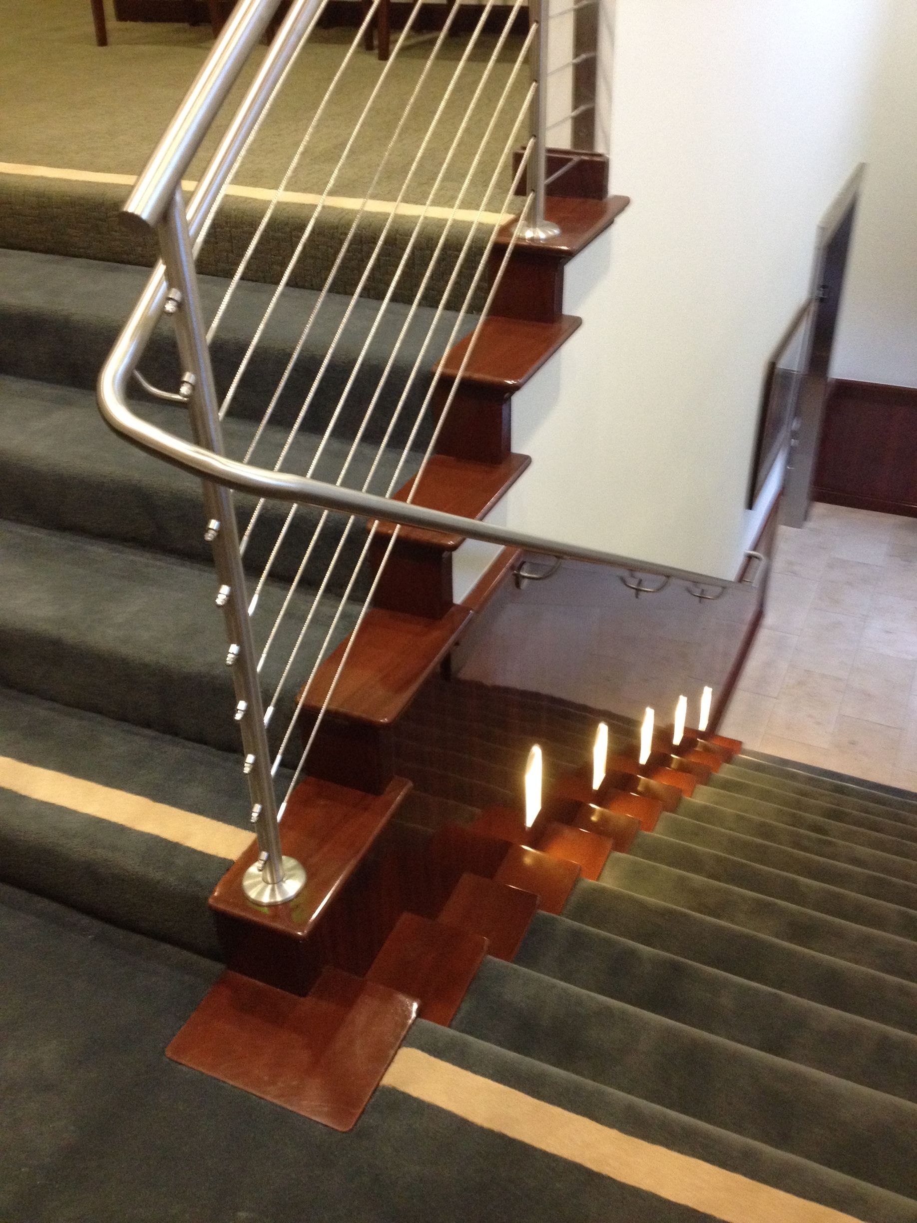 Staircase with wooden steps and metal railing. Carpeted stairs with lights along the side.