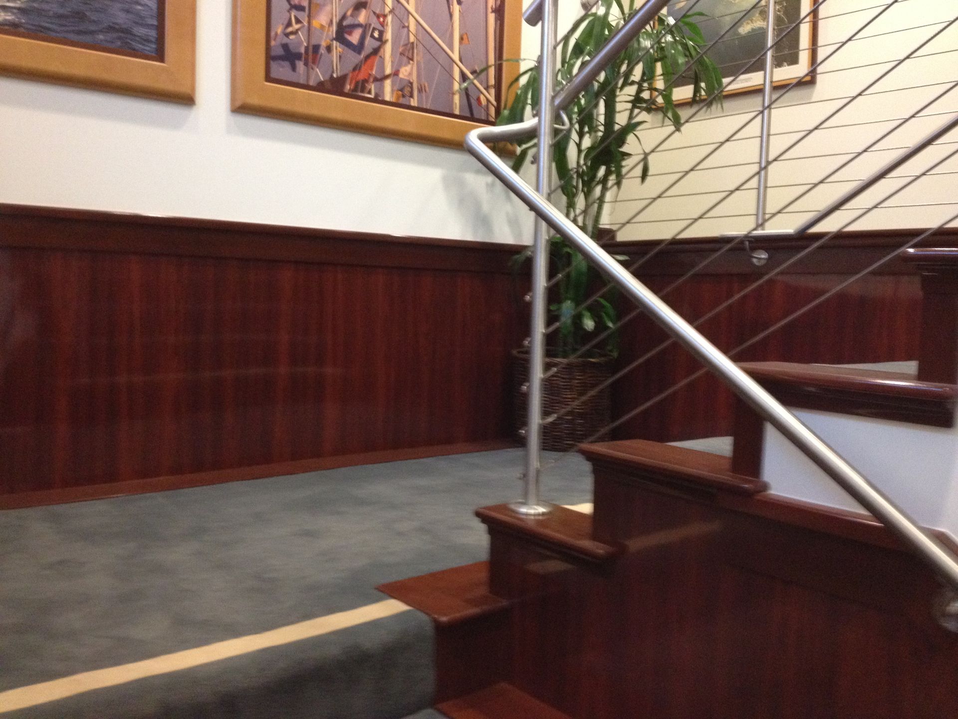 Wooden staircase with a stainless steel railing, featuring mahogany-colored paneling and a dark gray carpet.