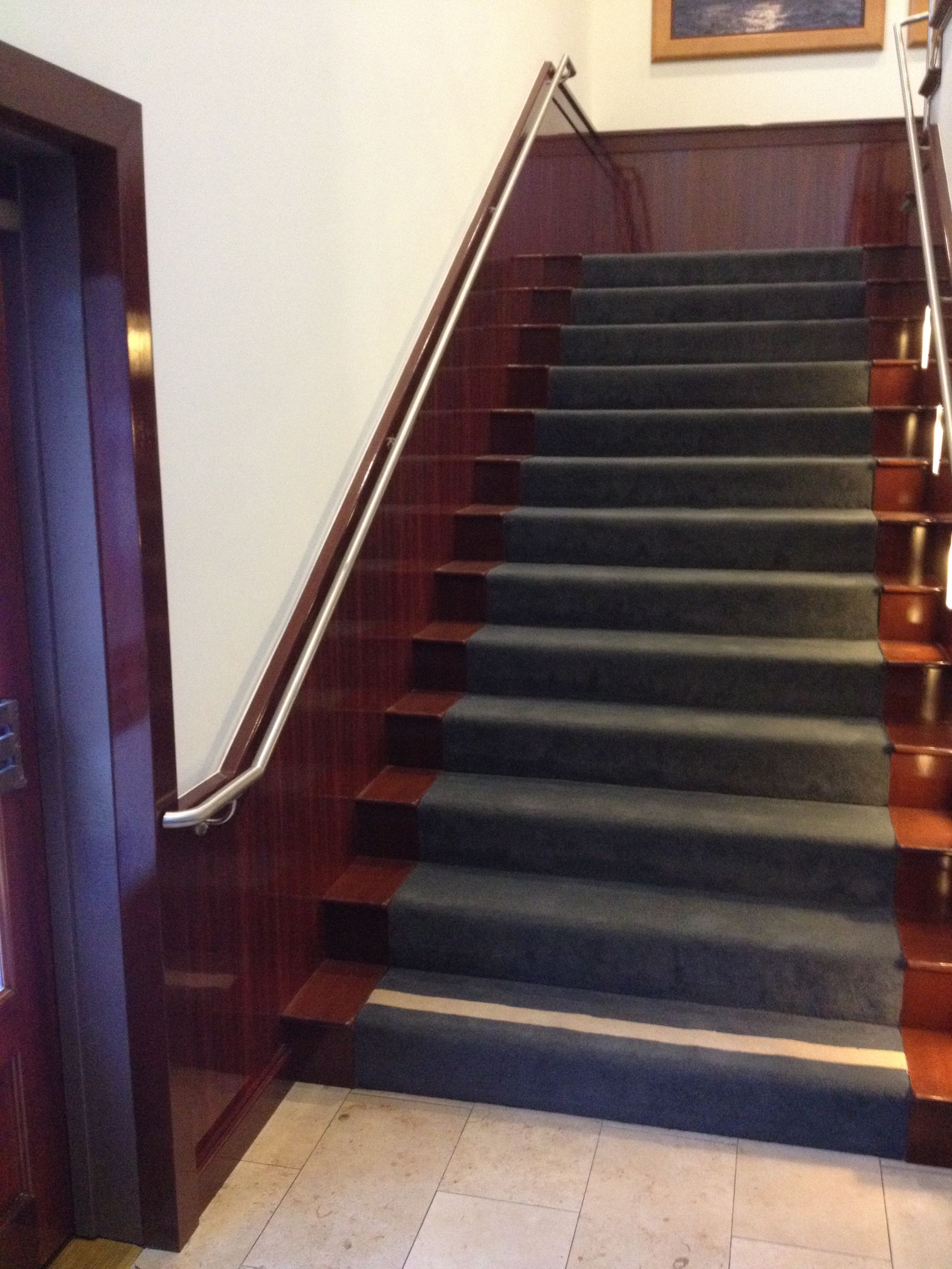 Staircase with dark red wood paneling, gray carpeted stairs, and a silver handrail.