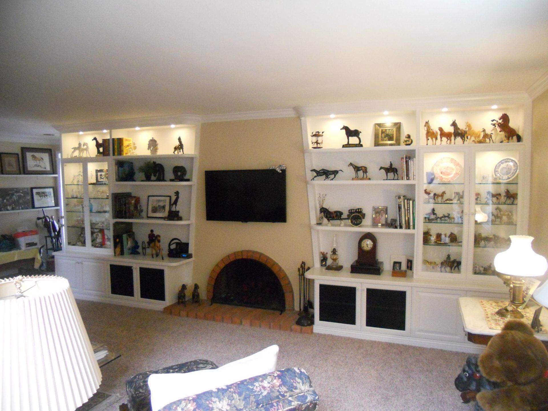 Built-in white bookshelves with displayed figurines surround a fireplace and TV in a living room.