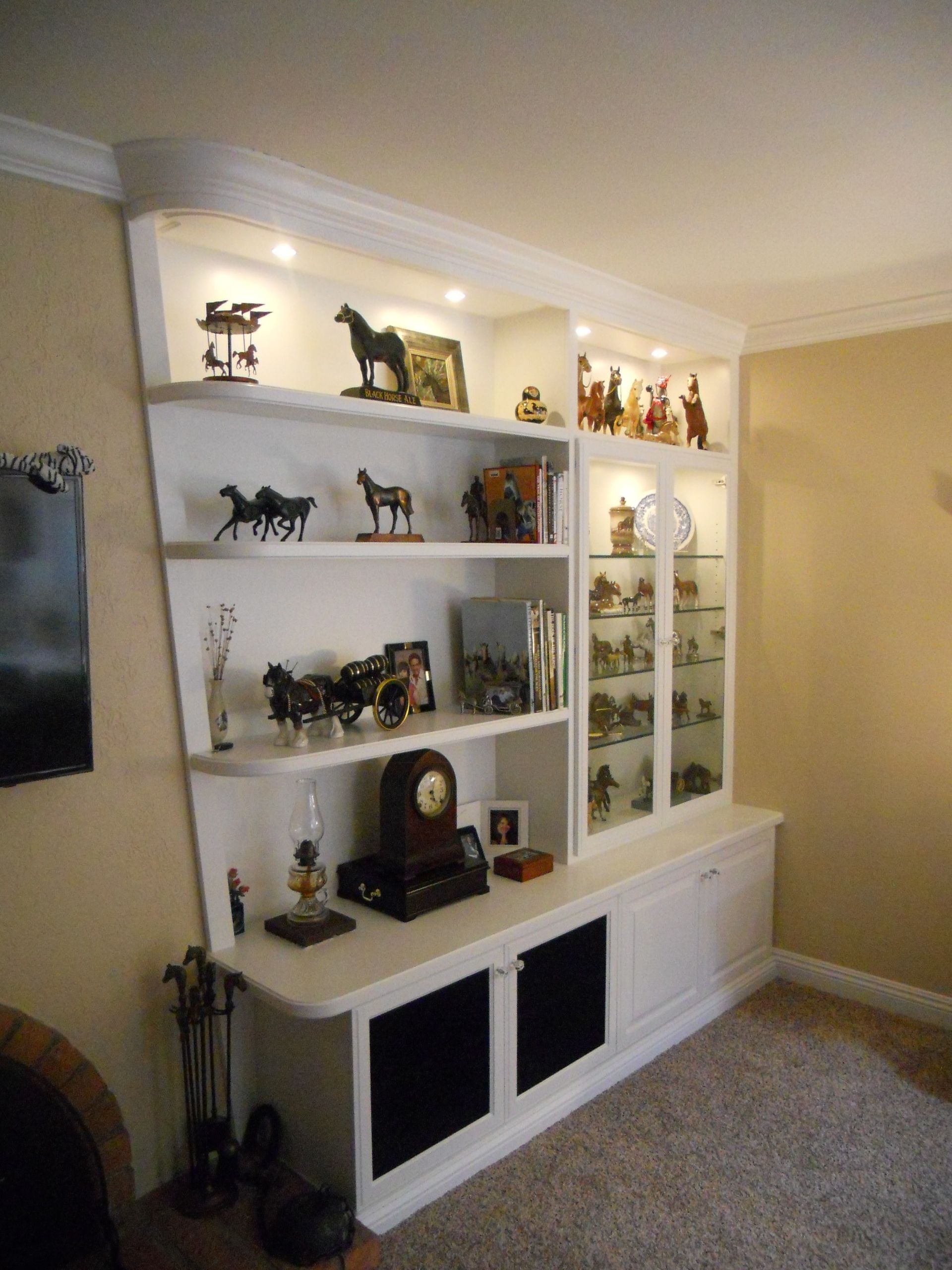White built-in shelving unit with decorative items, including horses and a glass display cabinet, against a beige wall.