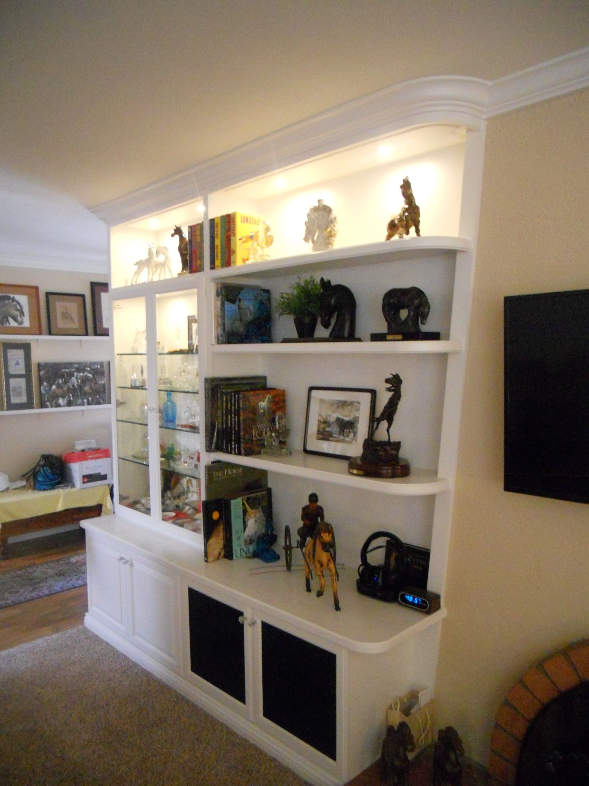 White built-in shelving unit with various decor: books, sculptures, and framed art. Recessed lighting.