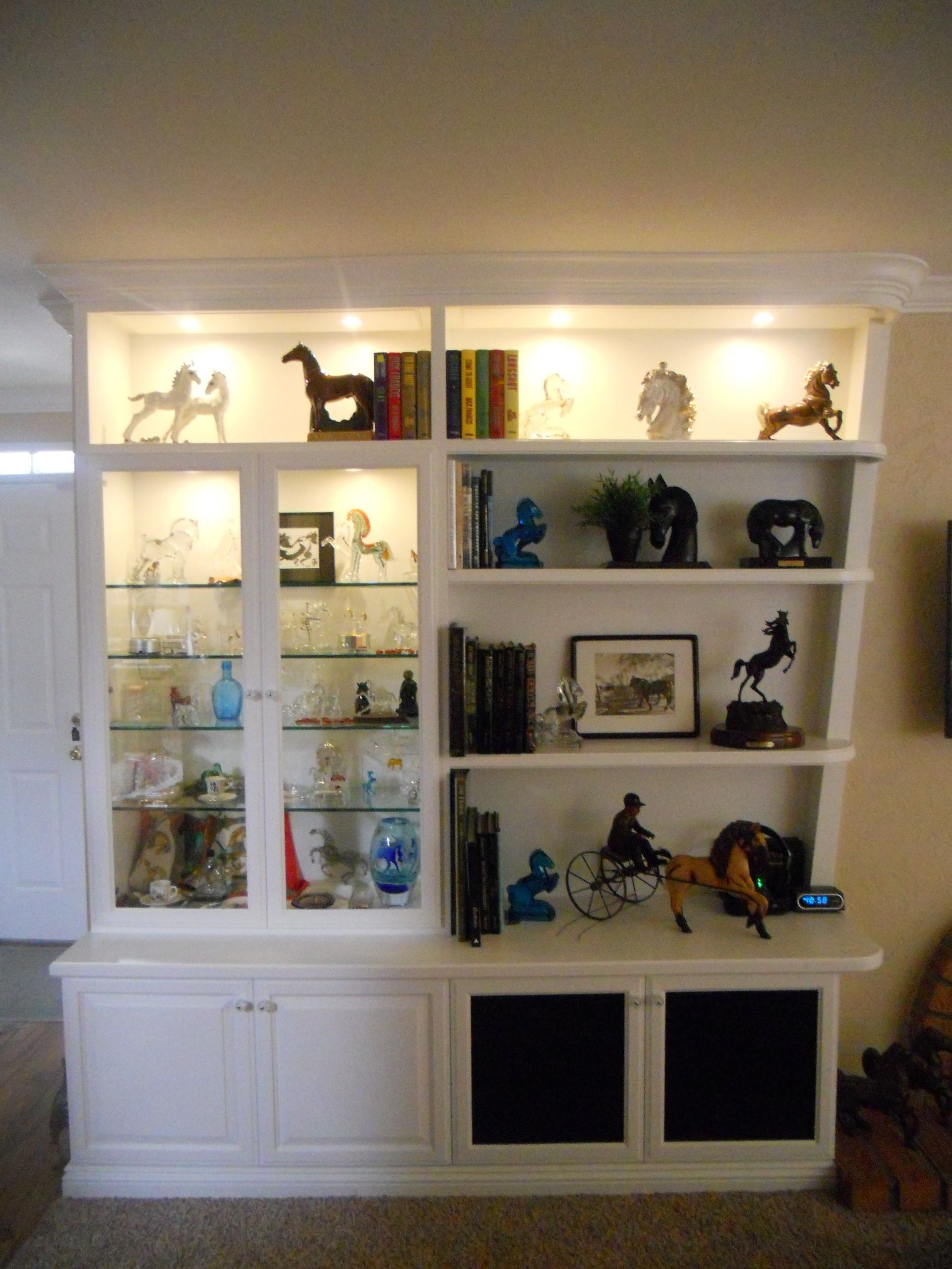 White built-in bookshelf with lit display shelves, featuring horse figurines, books, and decor.