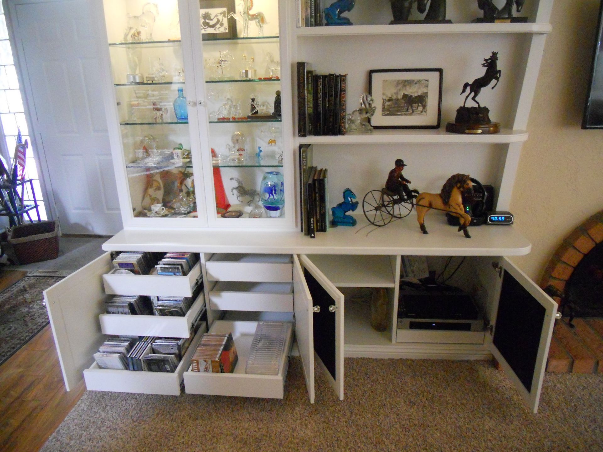 White cabinet with shelves, glass-fronted display, and drawers, holding figurines, books, and media.