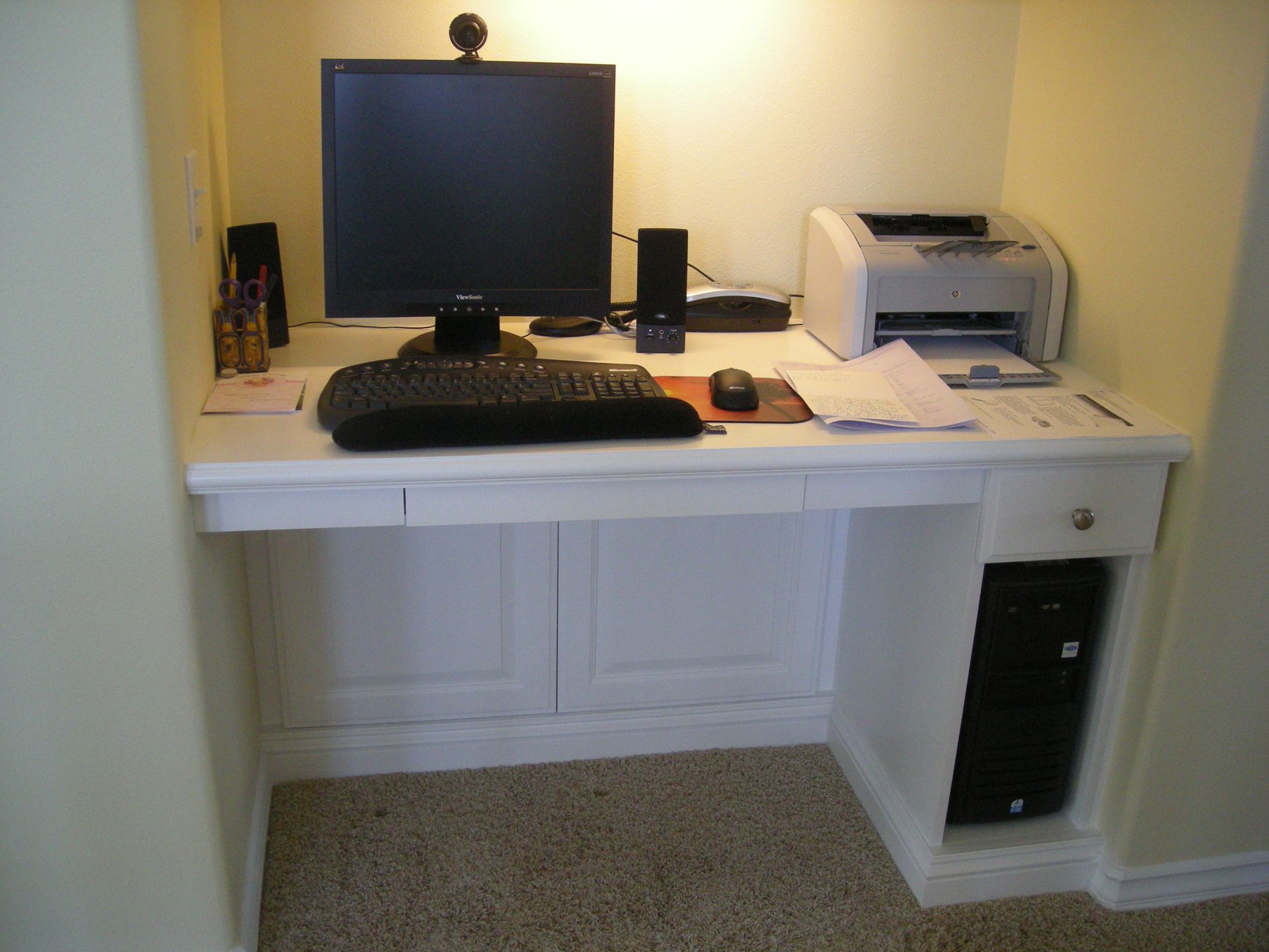 White built-in desk with computer, printer, and speakers in a recessed area.