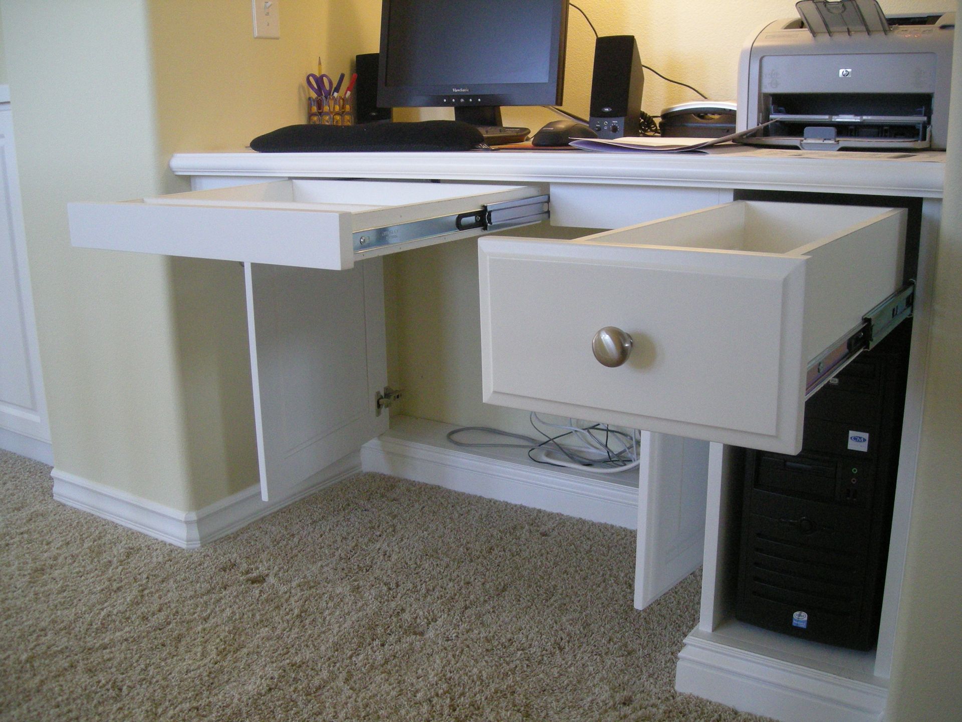 White built-in desk with open drawer, a computer tower, and a keyboard tray.