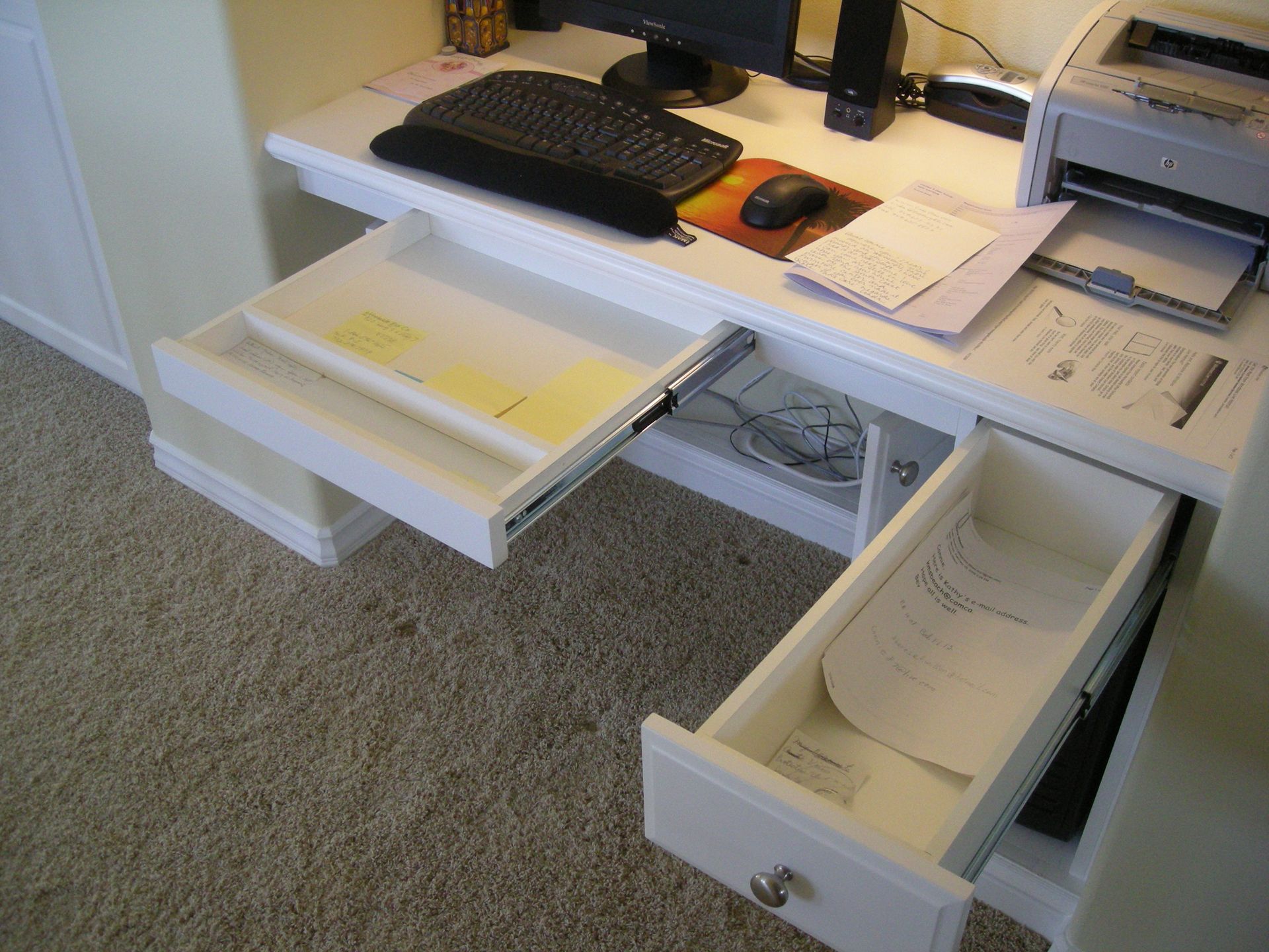 White office desk with open drawers. Keyboard, mouse, printer, and documents are on the desk.