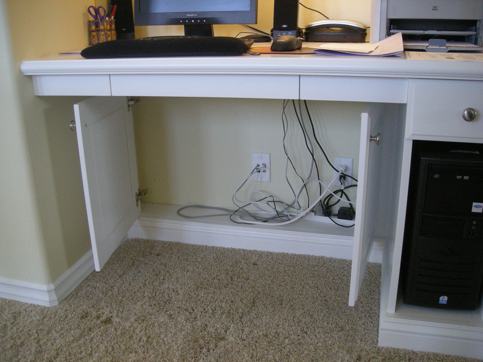 White desk with open cabinet doors, computer, and tangled cords.