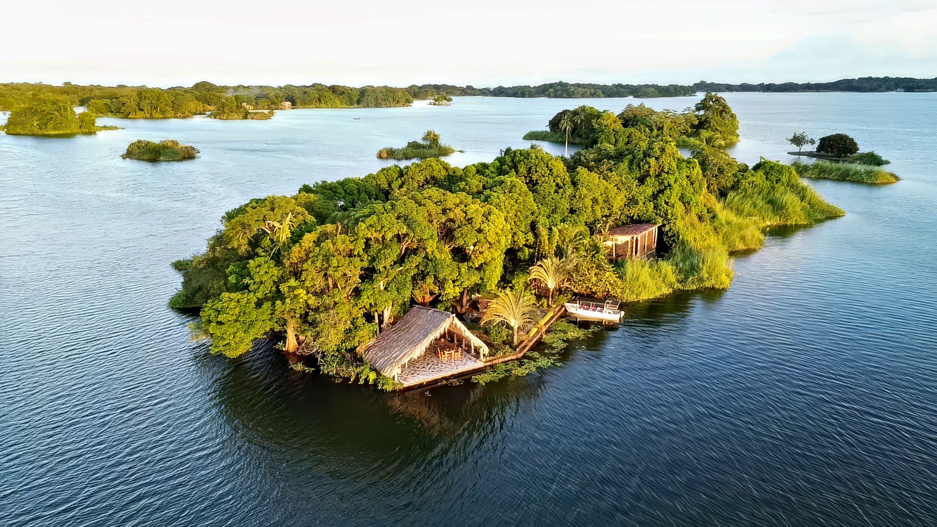 Island with lush green trees and structures surrounded by blue water.