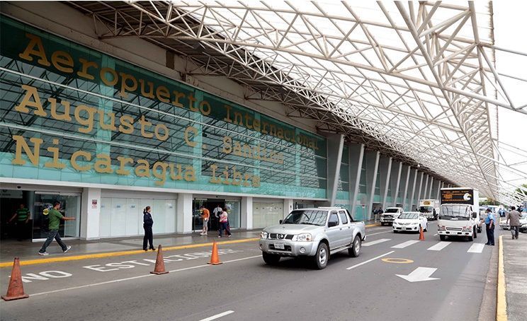 Airport exterior with a silver truck, people walking, and text 