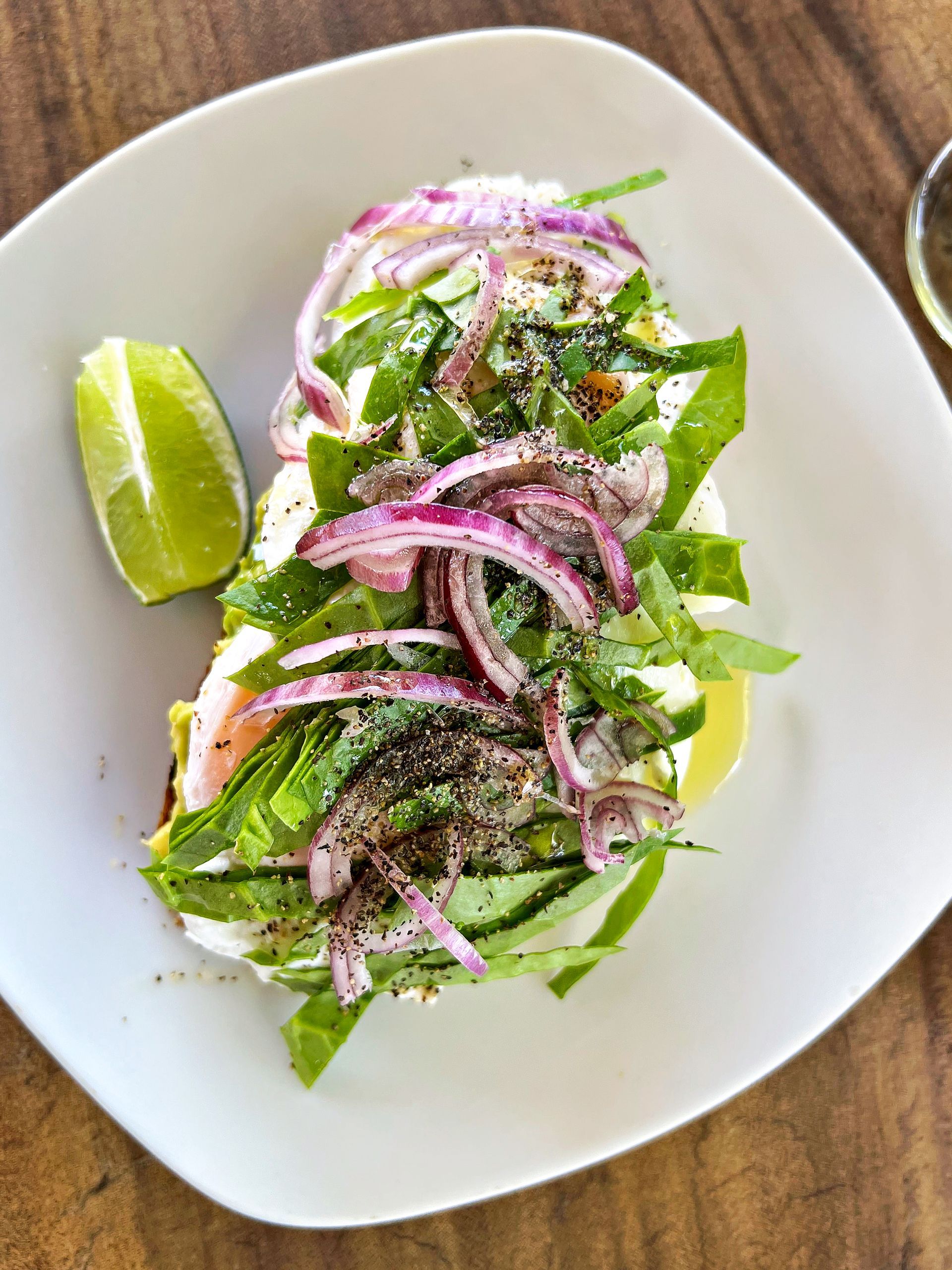 Toast topped with egg, red onion, herbs, and lime wedge on a white plate.