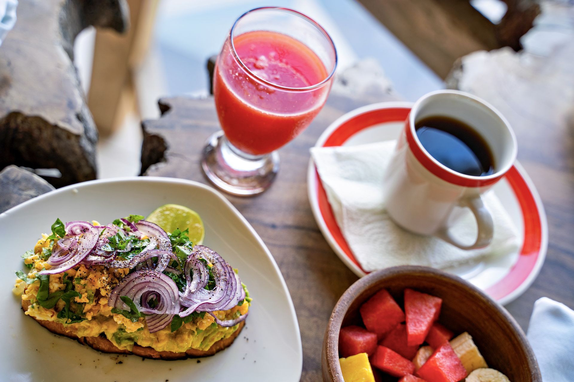 Breakfast spread with avocado toast, fruit bowl, coffee, and juice.