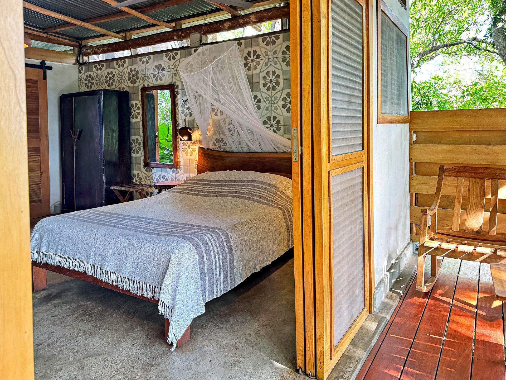 Bedroom with bed, wooden shutters, dark cabinet, and outdoor seating on a deck.