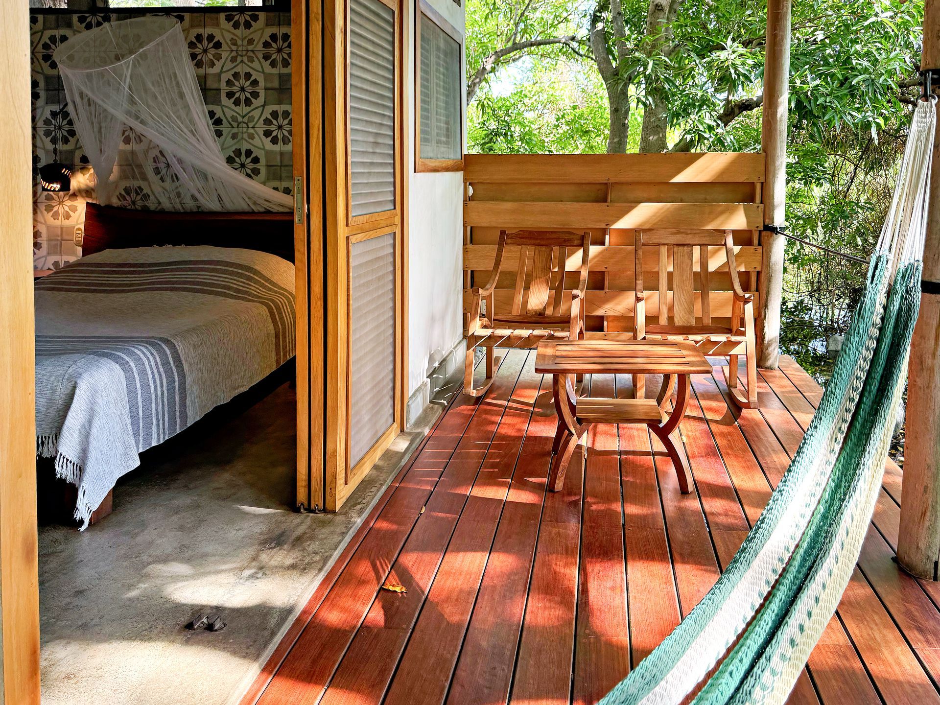 Bedroom with porch, featuring a bed, wooden bench, table, and a hammock.