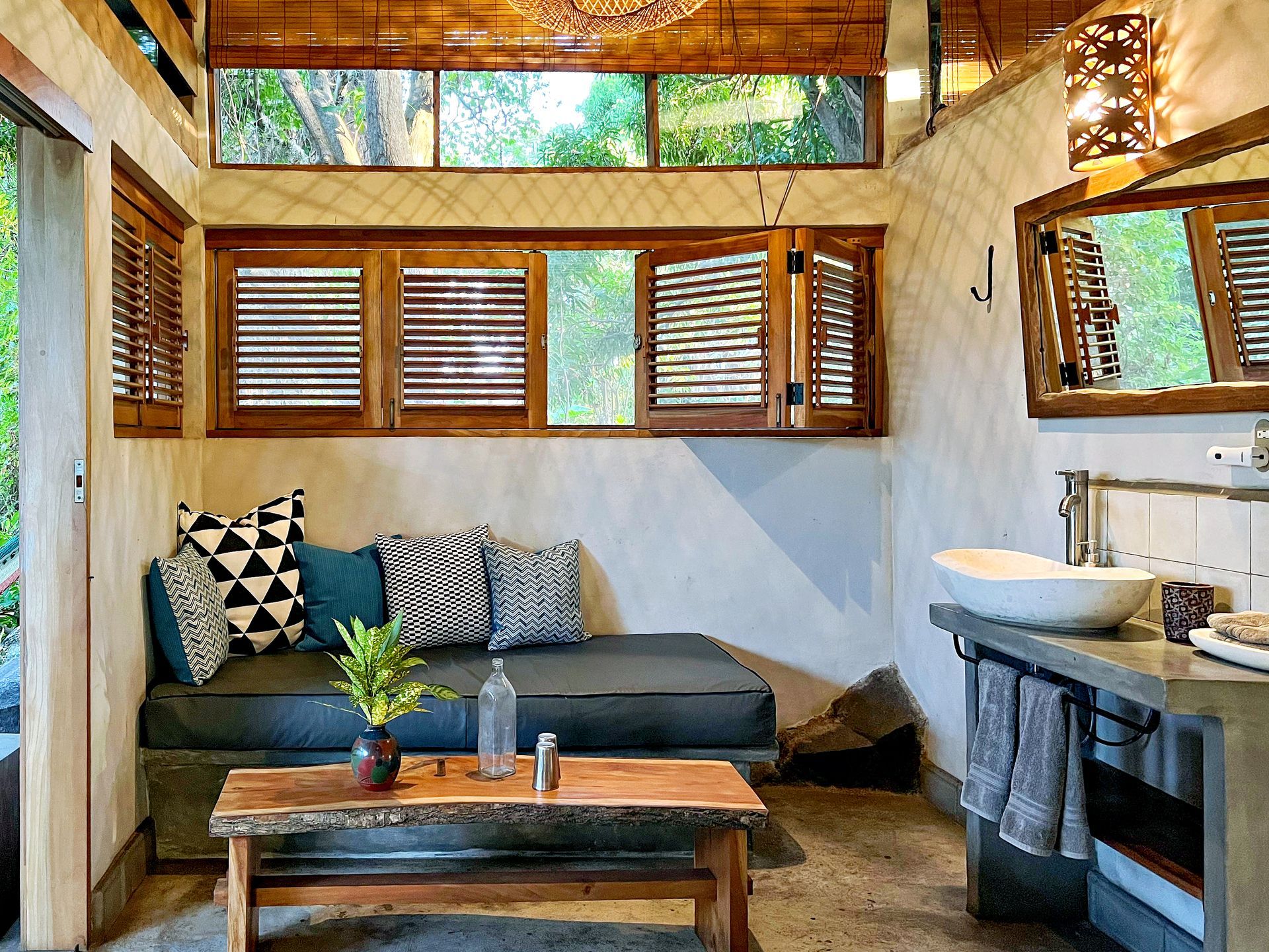 Cozy room with a couch, wooden table, and bathroom counter with a sink. Natural light streams through the windows.