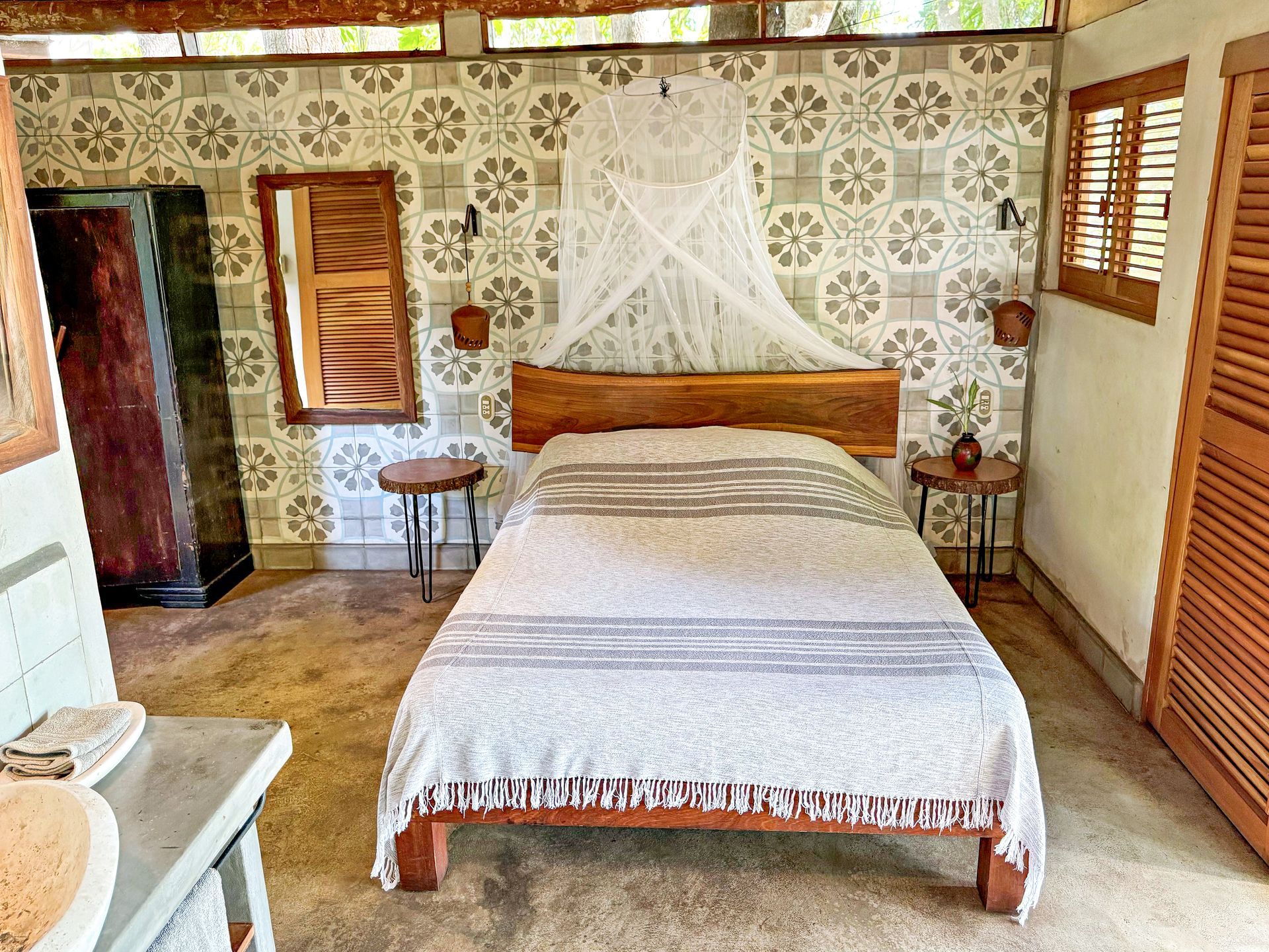 Bedroom with patterned wallpaper, wooden bed, and side tables, mosquito net.
