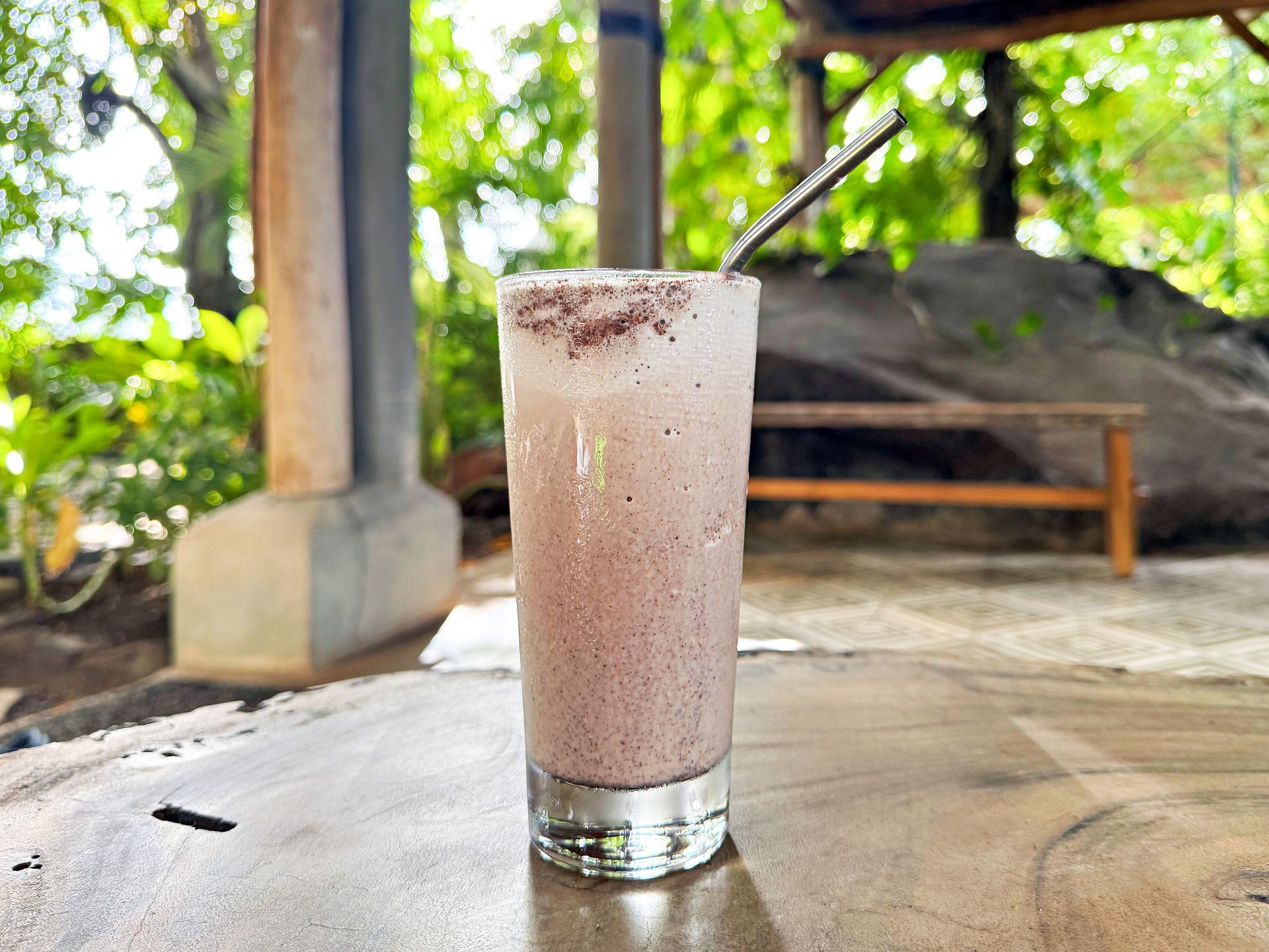 Glass of purple smoothie with a straw on a wood table, outdoor setting.