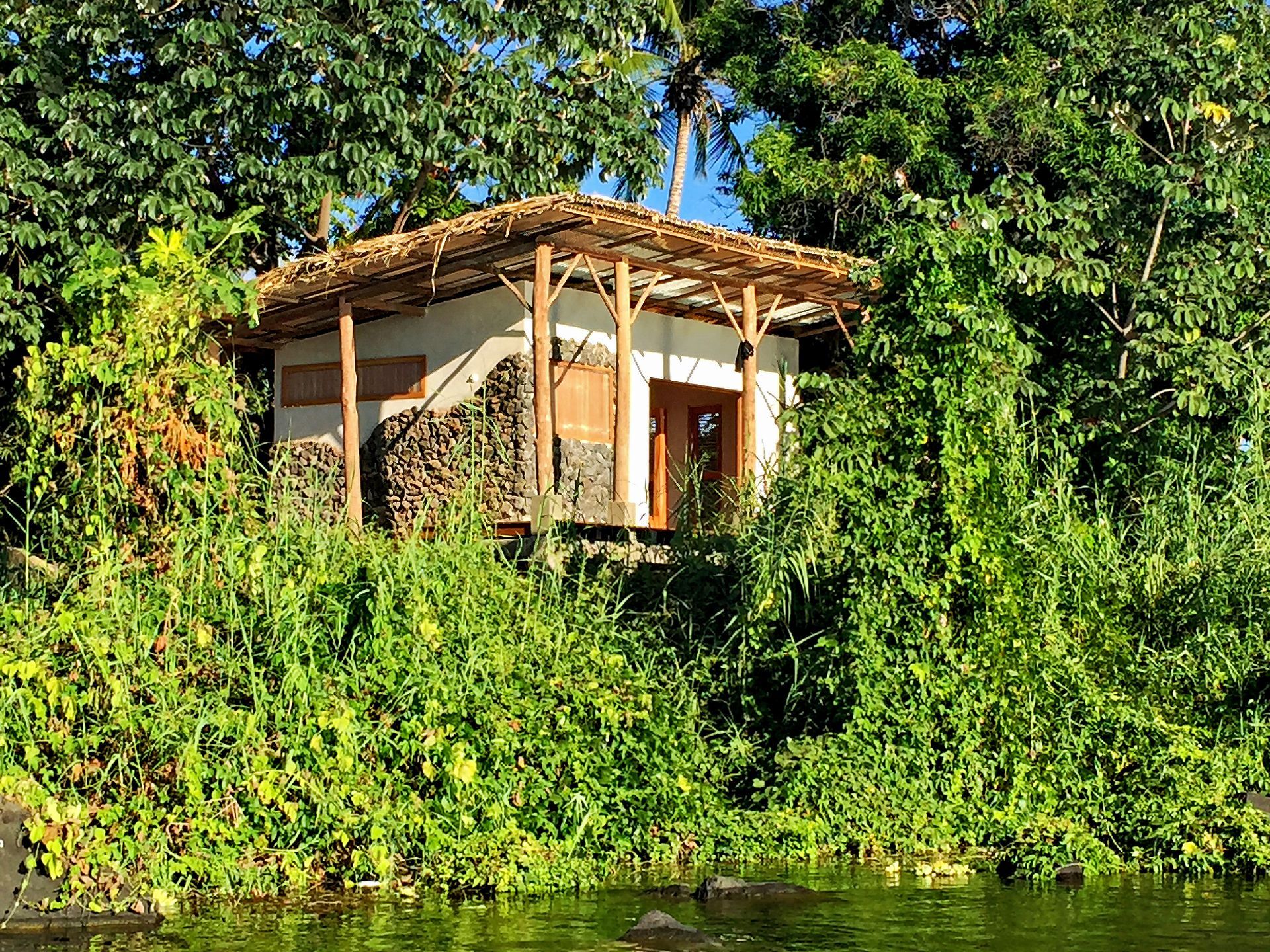 Small cabin surrounded by lush green vegetation on a riverbank.