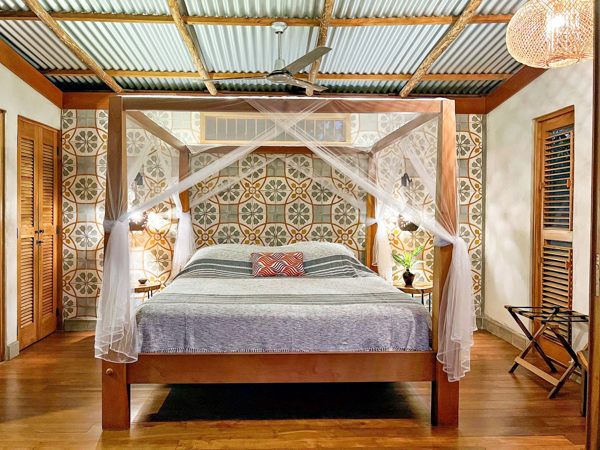 Bedroom with canopy bed, patterned accent wall, wood floors and ceiling, with a fan and decorative lighting.