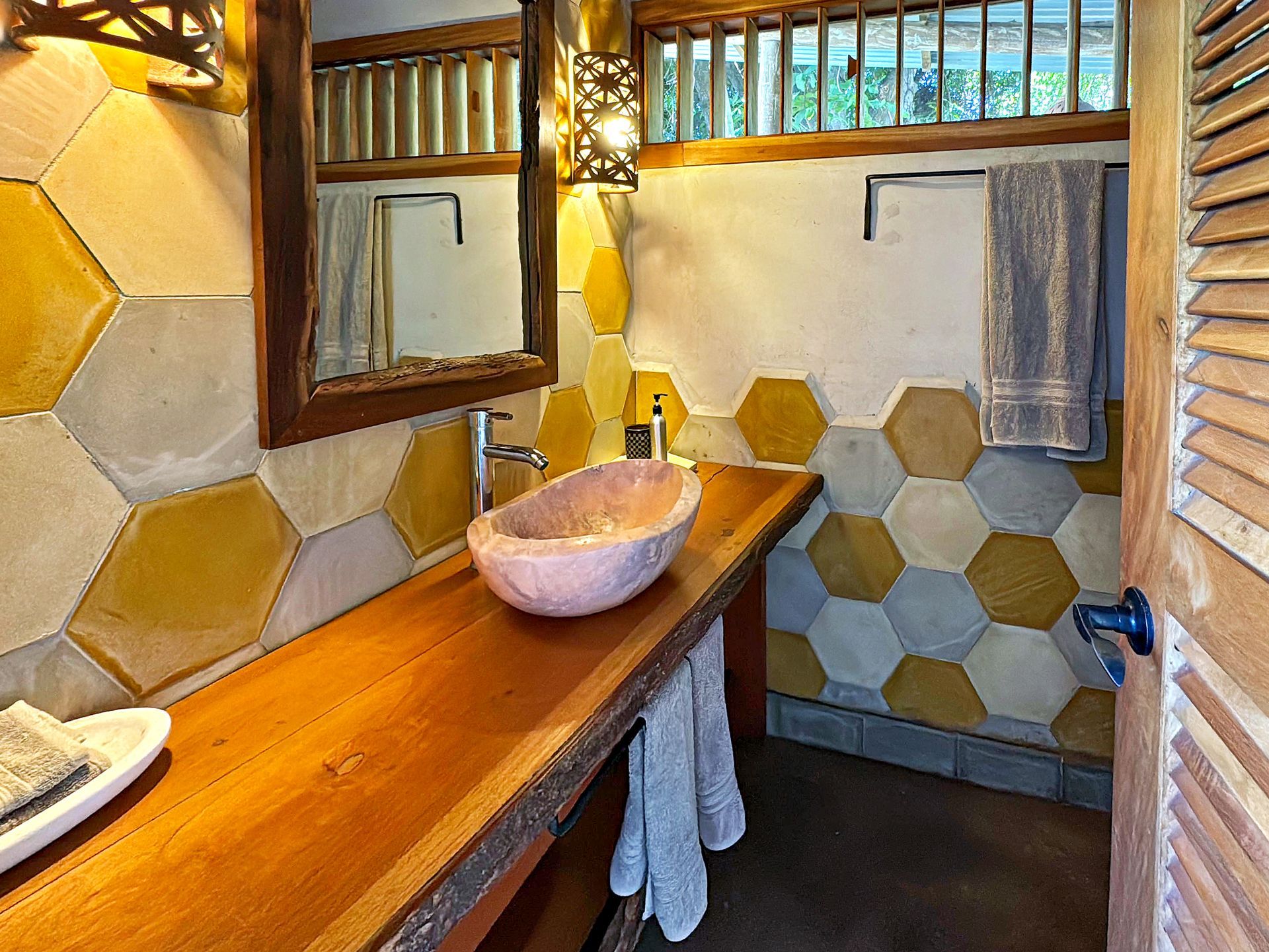 Rustic bathroom with wooden counter, pink basin, and honeycomb-tiled walls in yellow and gray.