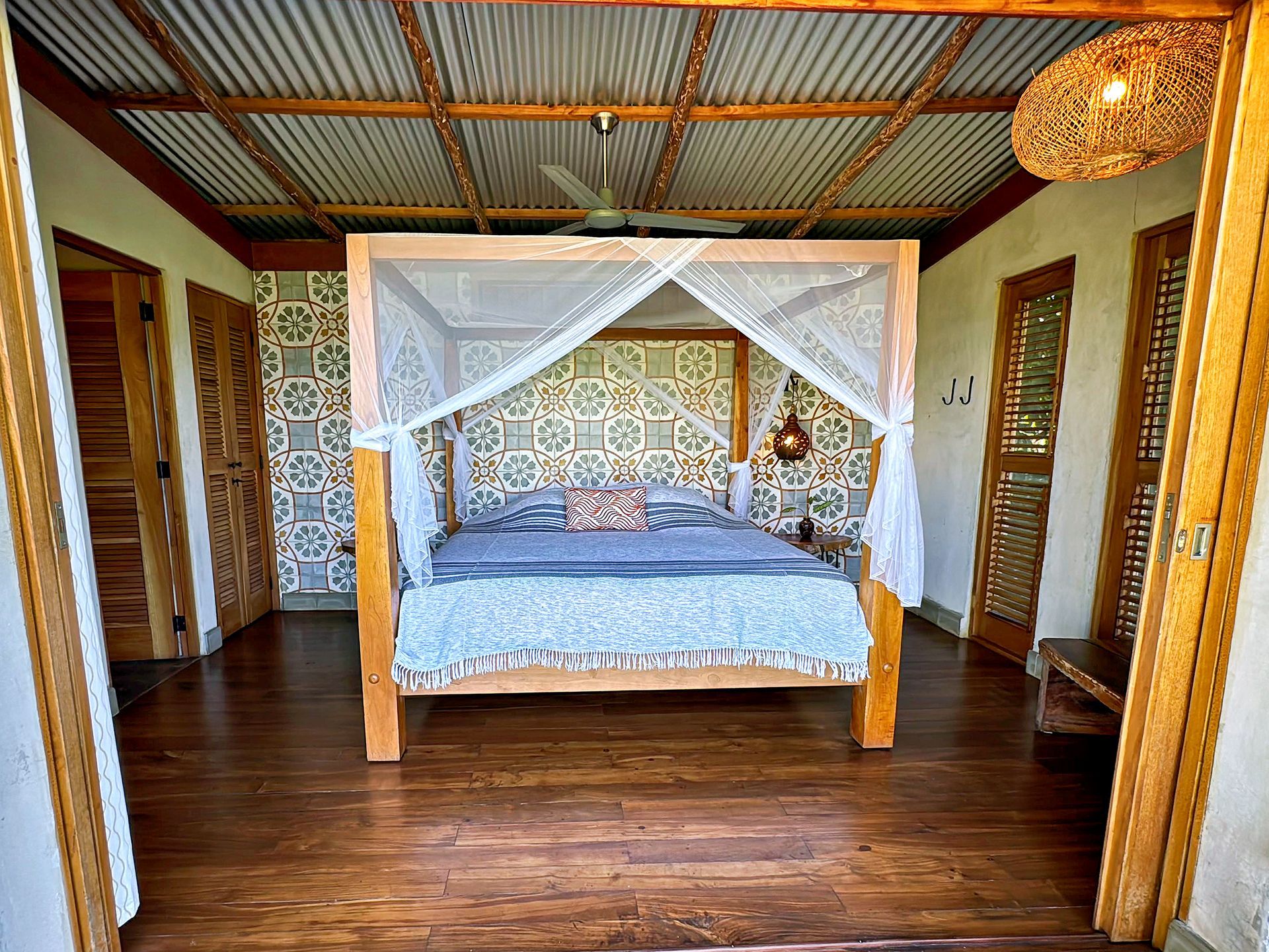 Bedroom with canopy bed, patterned wallpaper, wood floors, and open doors.