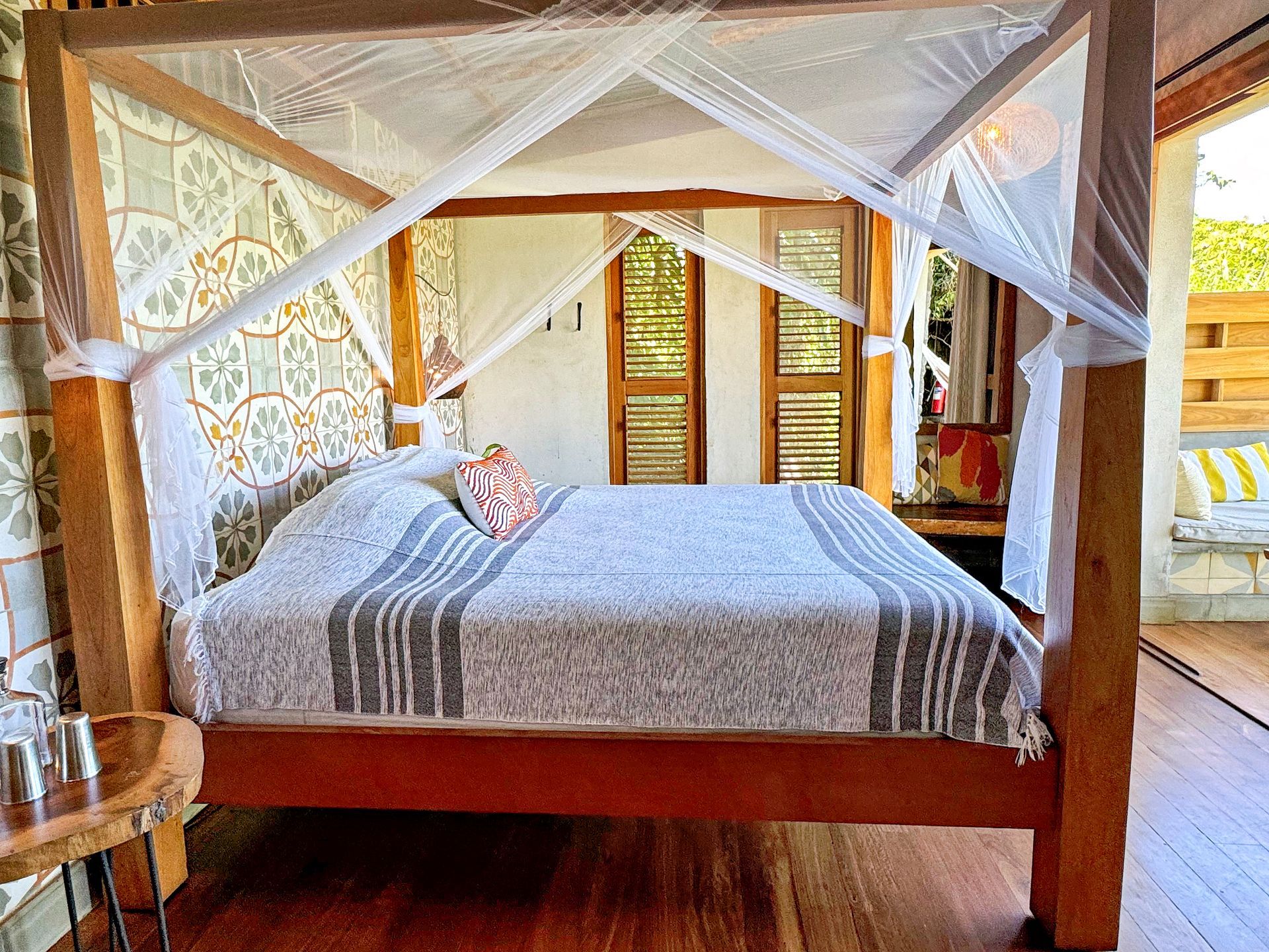 Bedroom with a four-poster bed draped with mosquito netting; patterned tile wall.