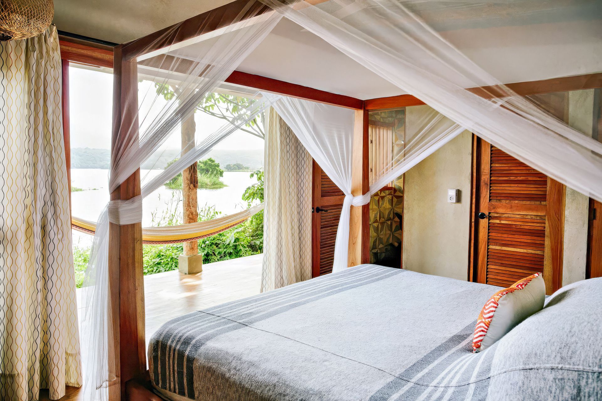 Bedroom with a canopy bed, a view of the water, and a hammock on the balcony.
