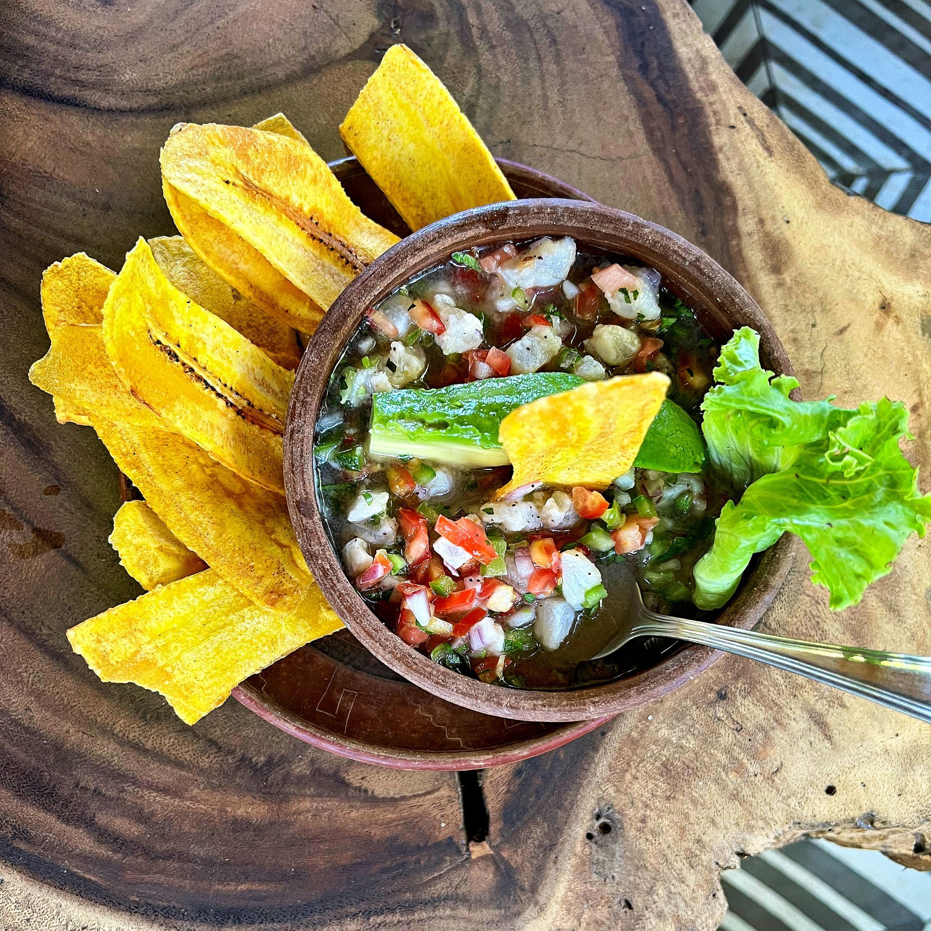 Shrimp ceviche in a bowl with plantain chips on a wood slab.