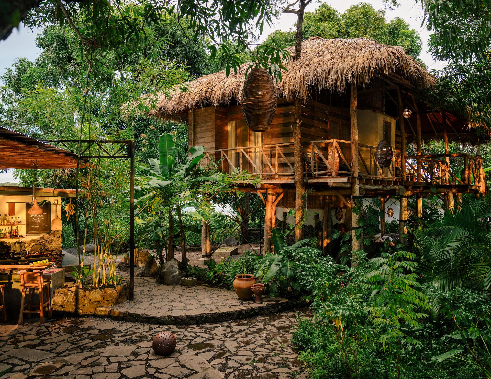 Wooden treehouse with thatched roof amidst lush greenery.