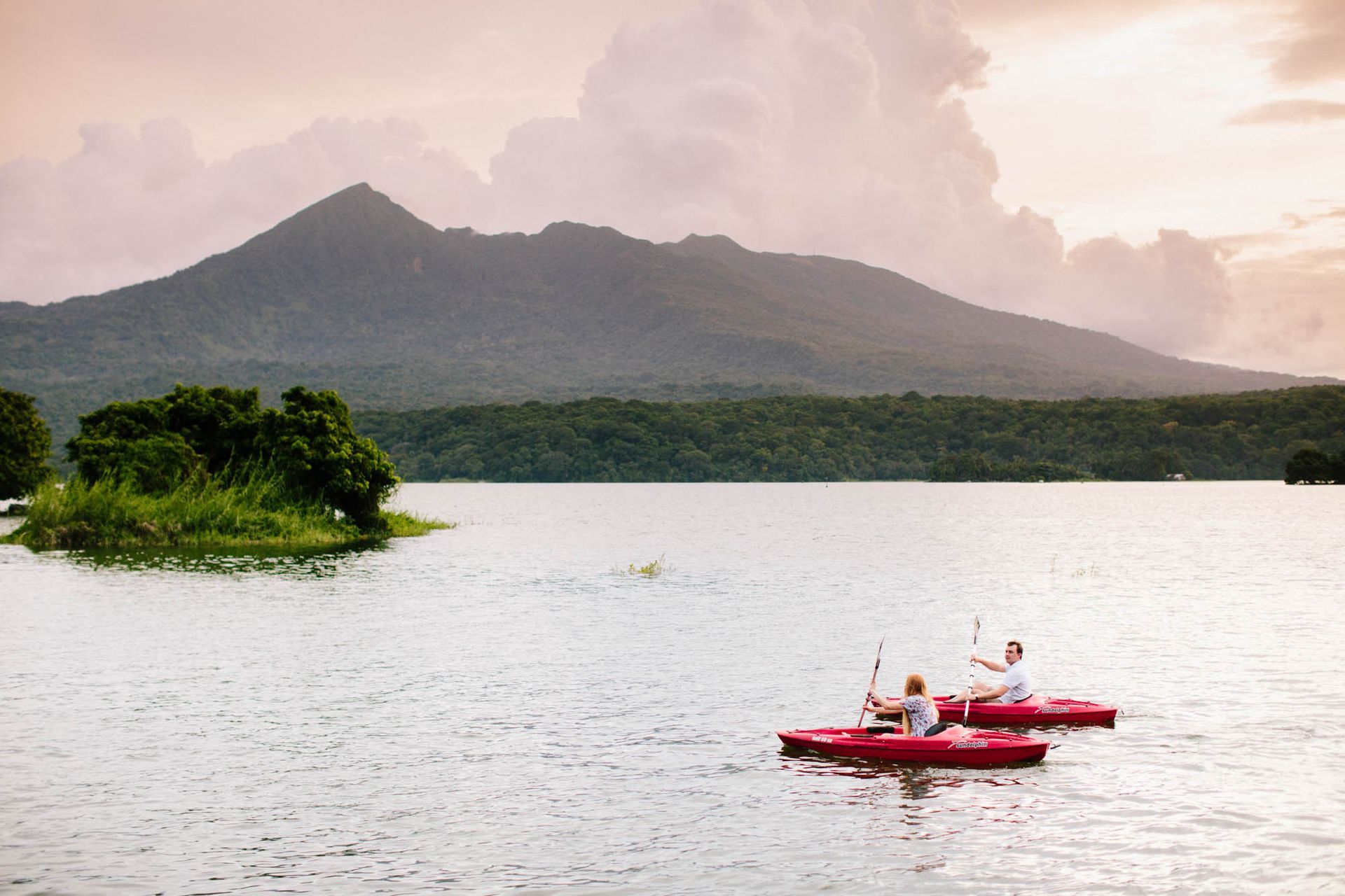 Two people kayaking on a lake with a mountain in the background, cloudy sky, red kayaks.