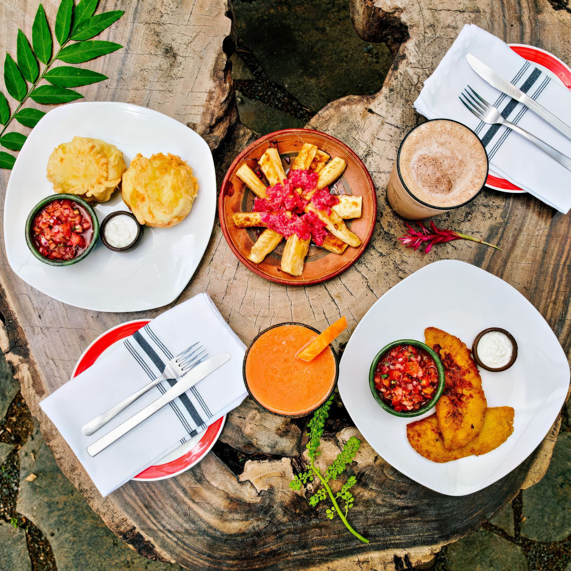 Breakfast spread on a wood table: empanadas, yucca fries, plantains, drinks, and condiments.