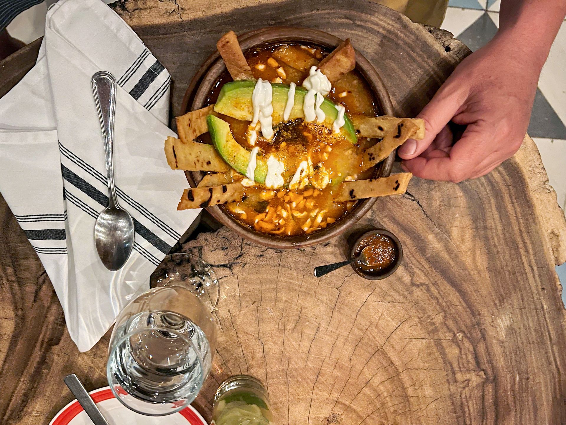 Bowl of soup with avocado, tortilla chips, and crema on a wooden slab.