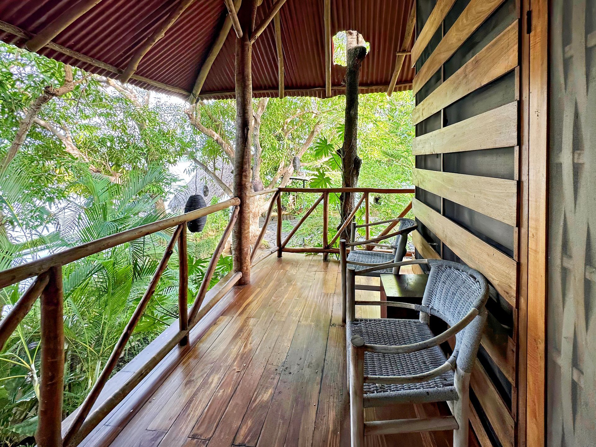 Wooden balcony with seating overlooking lush green trees.