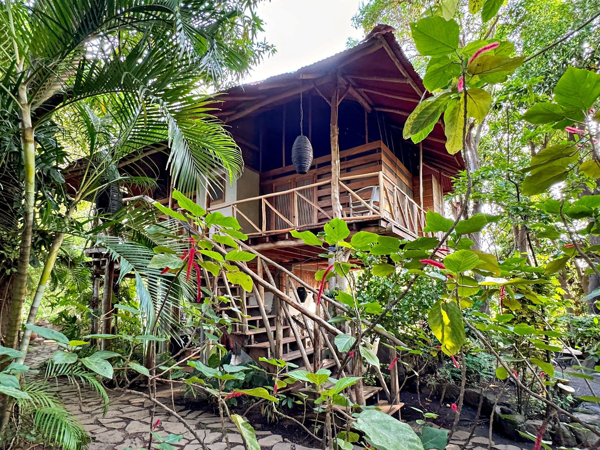 Wooden treehouse with a balcony, surrounded by lush green vegetation.