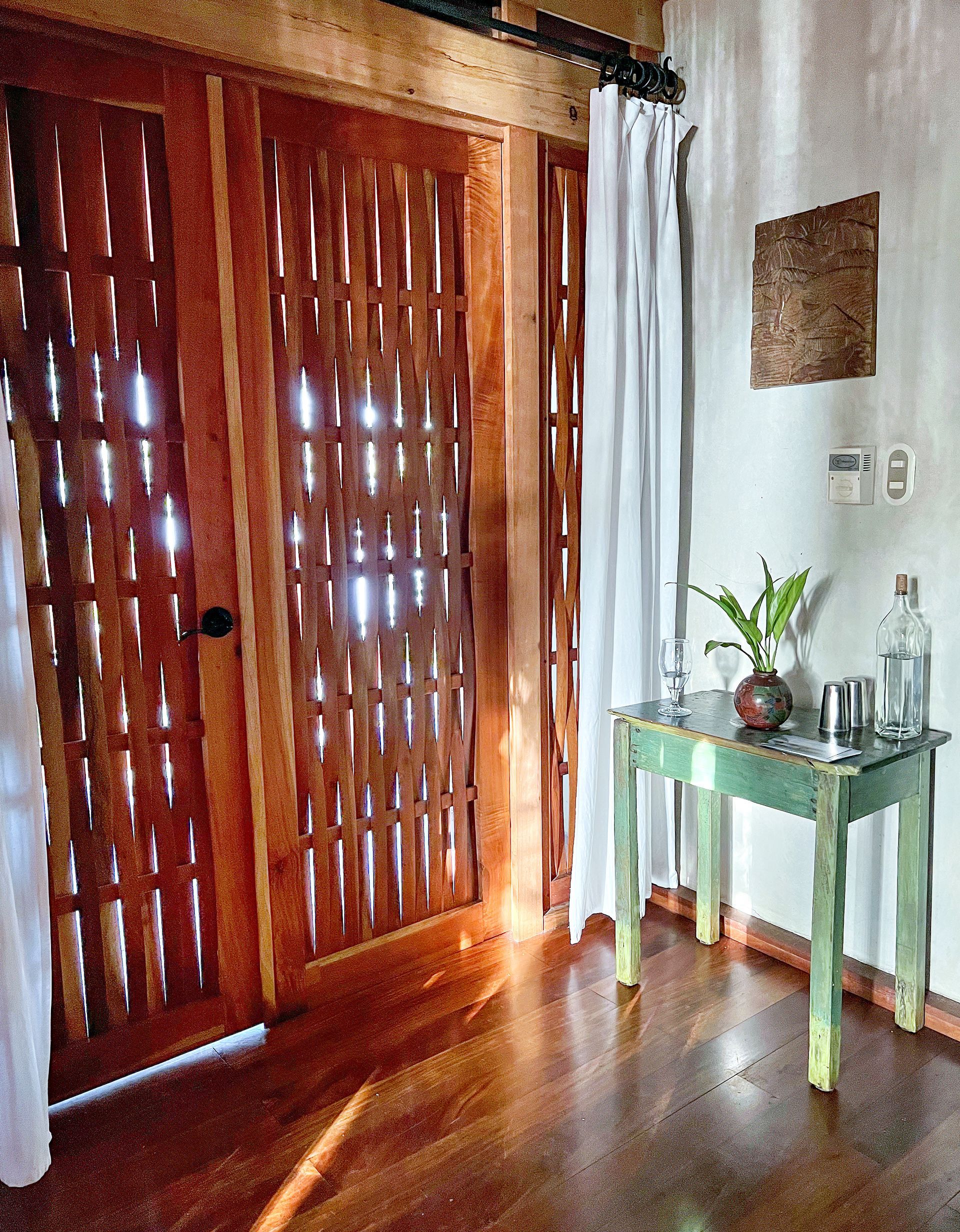 Wooden door with decorative slats, next to a white curtain, and a small green table with items.