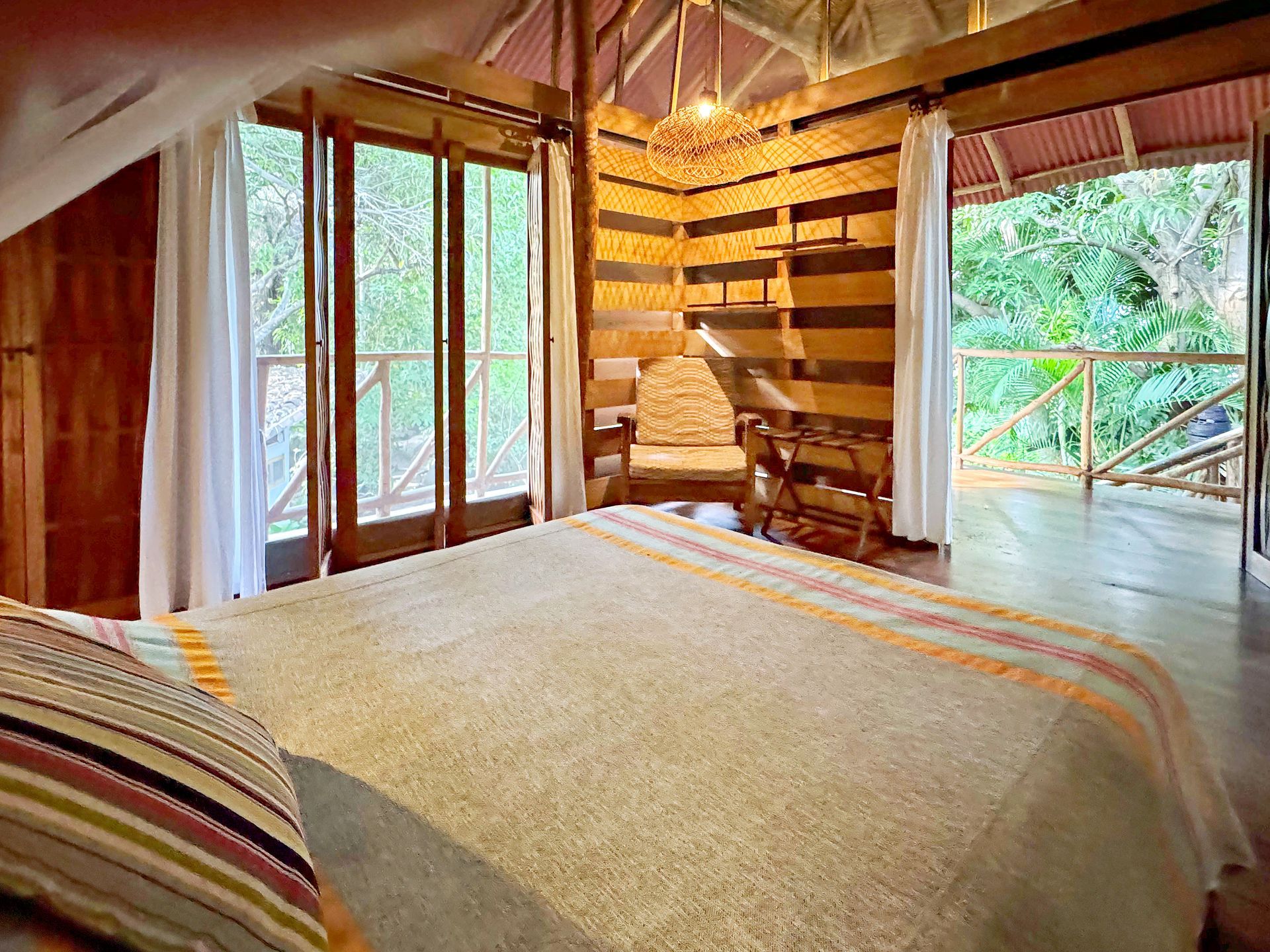 Cozy wooden bedroom with a bed and open doors leading to a deck and lush greenery.